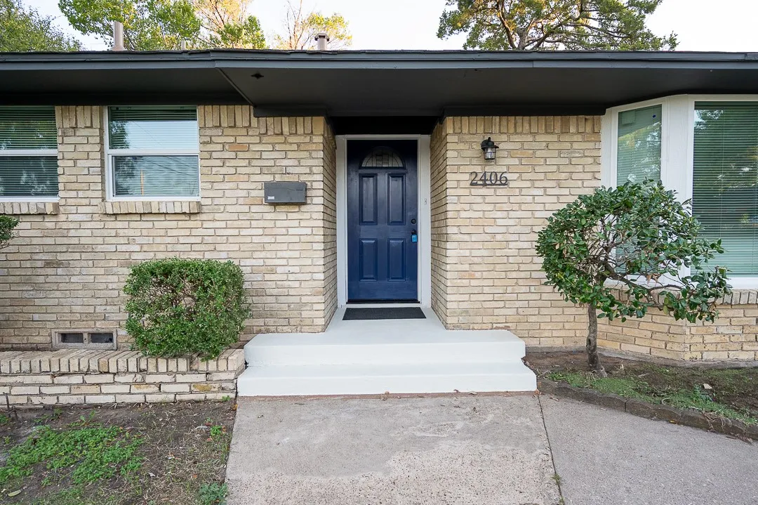 Exterior facade featuring light-toned brick masonry, a blue-painted front door with arched glass detail, and a bay window