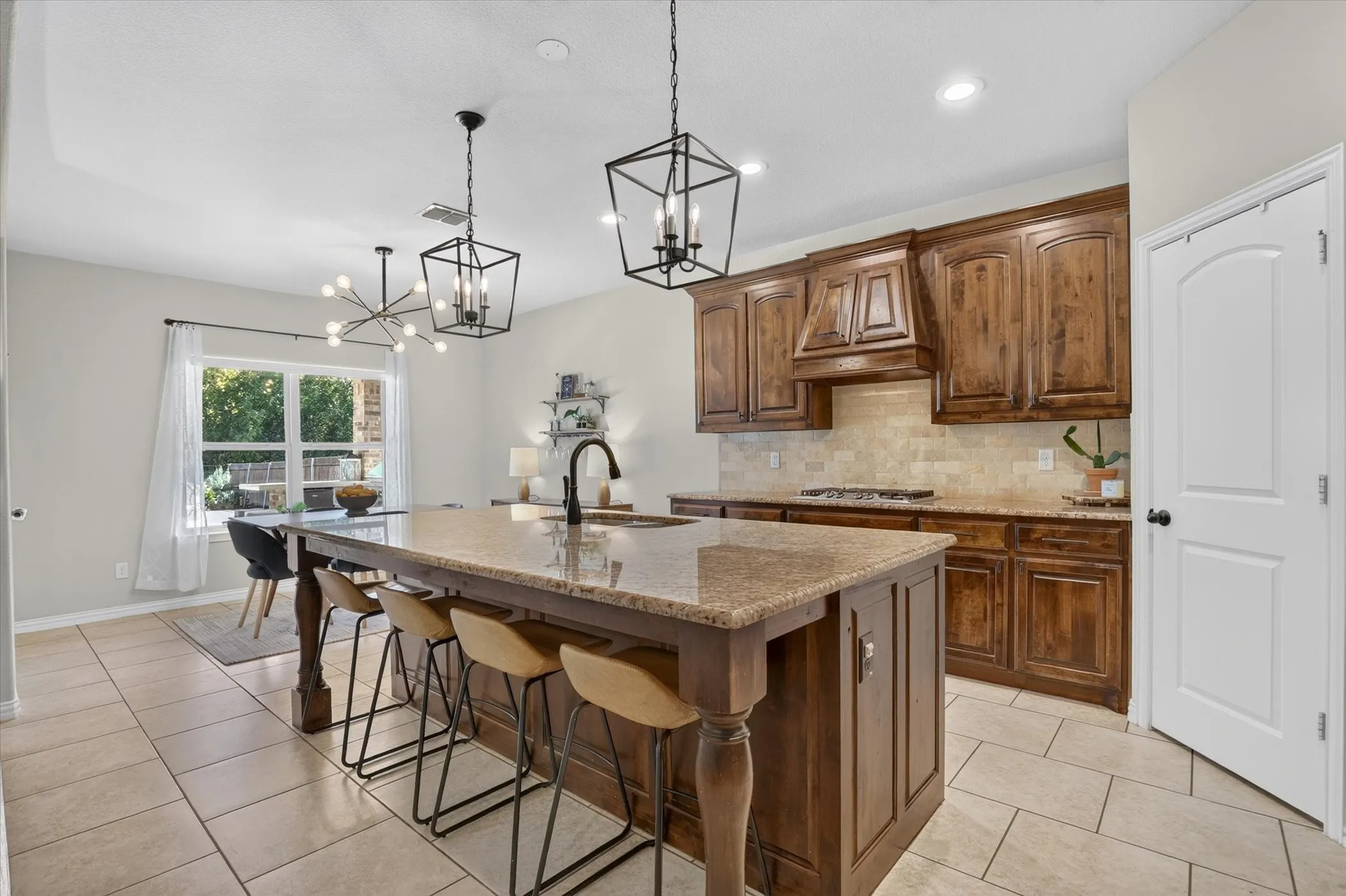 Kitchen featuring stained wood cabinetry, stone-surface countertops, central island with seating, stone backsplash, and multi-light geometric pendant fixtures