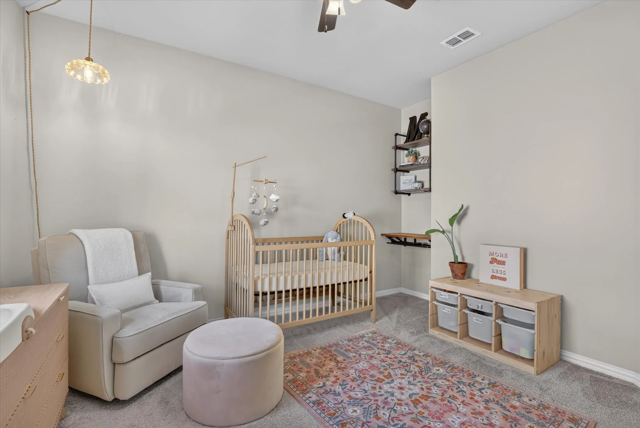 Room featuring neutral wall tones, neutral carpeting, industrial-style wall-mounted shelving with wood-finish planks, a multi-light ceiling fan, and a suspended pendant light fixture