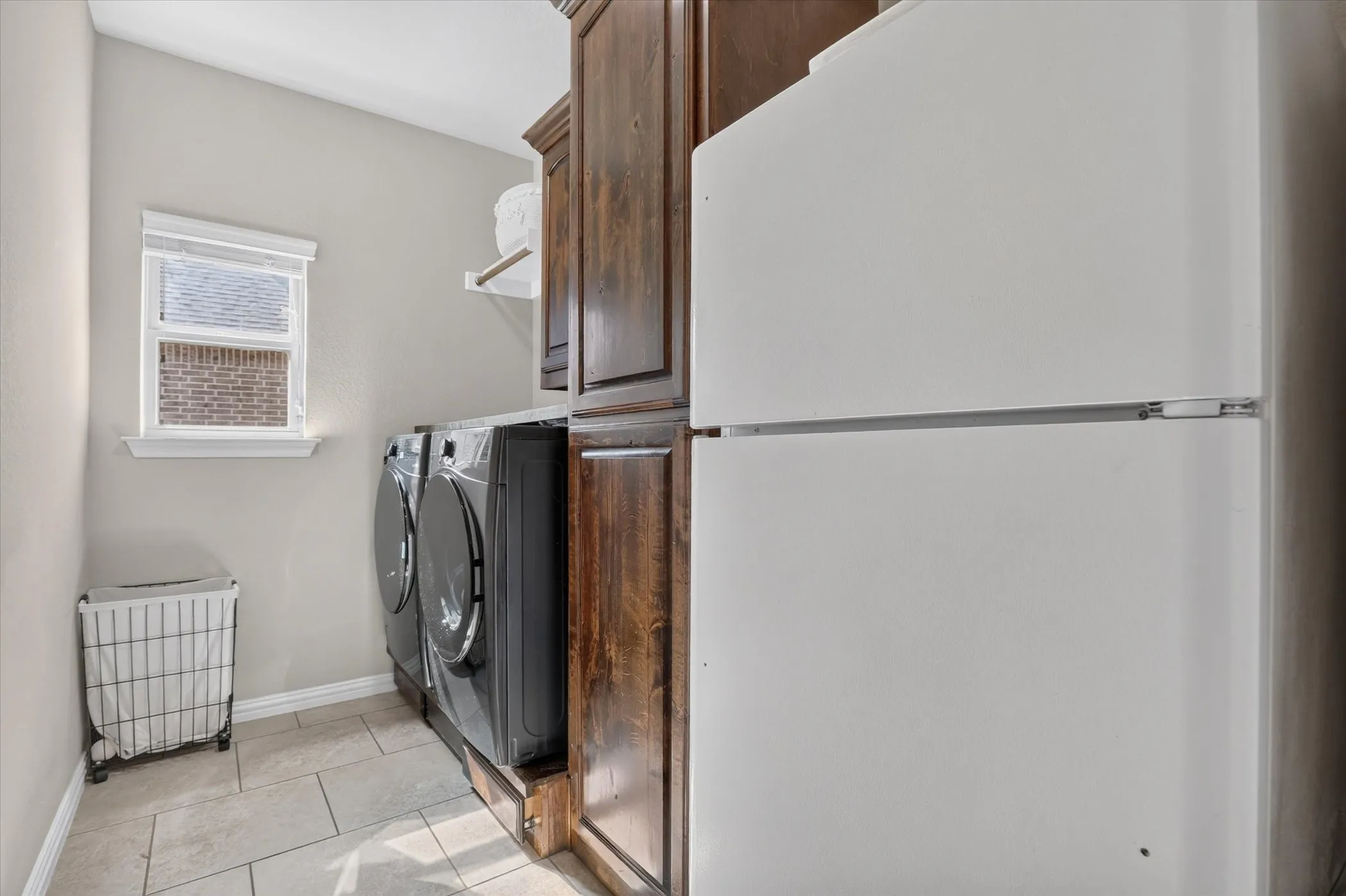 Laundry area featuring dark wood-finish cabinetry, a built-in hanging rod, tile flooring, and a single-pane window
