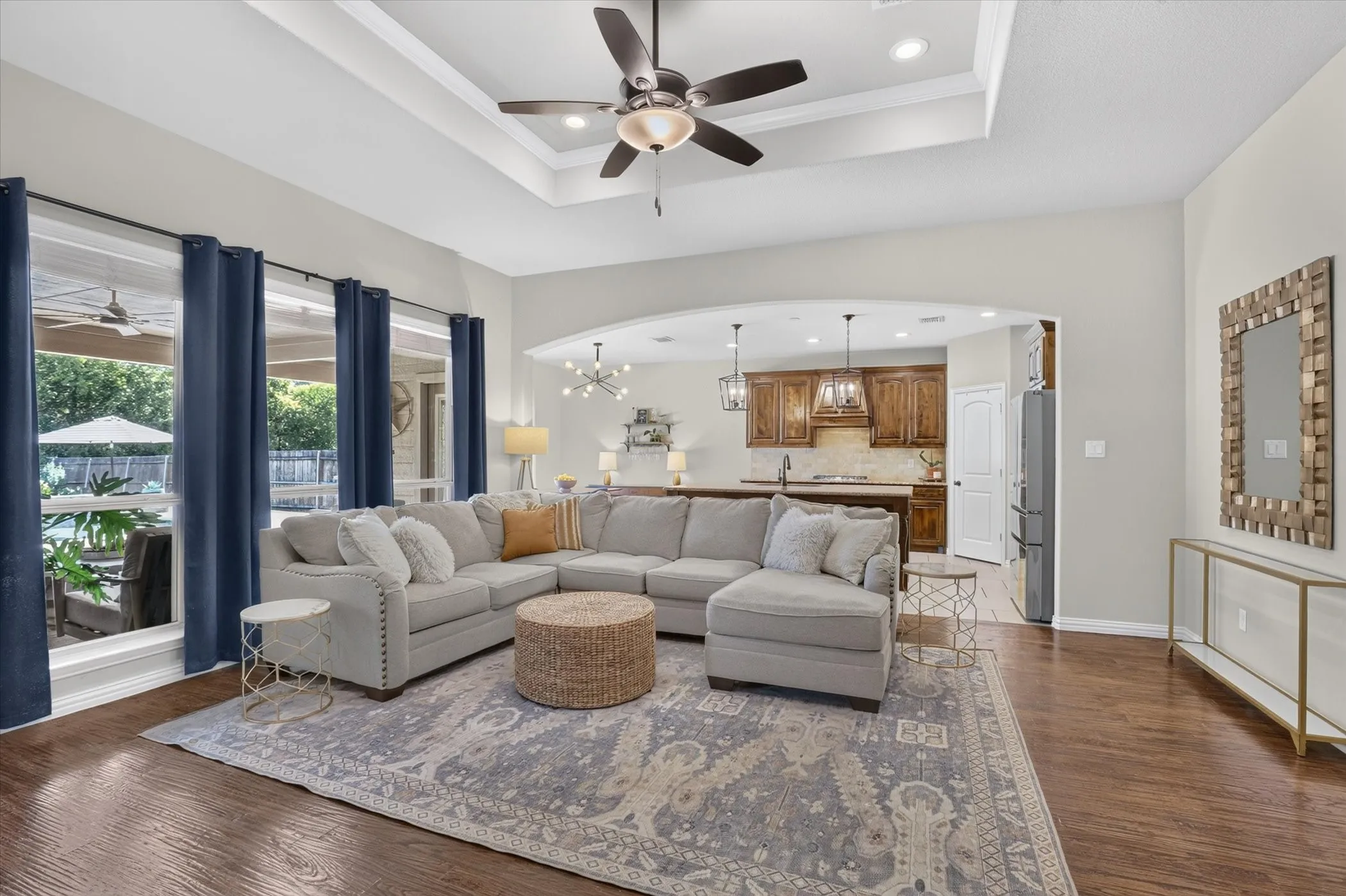 Tray ceiling with recessed lighting, wood-finish flooring, arched entryway, and large windows with natural light