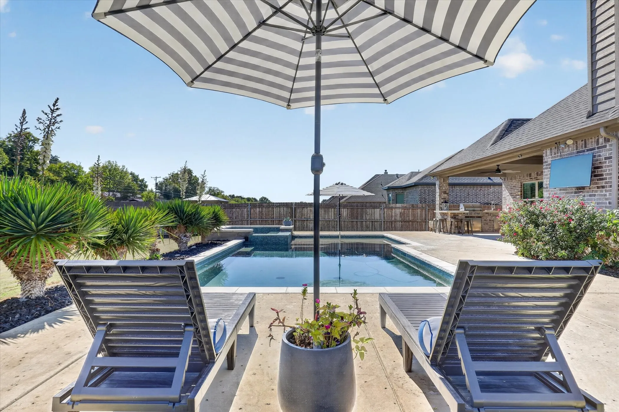 Concrete patio featuring a rectangular swimming pool with an integrated spa, covered outdoor kitchen with stone veneer, and perimeter wood privacy fencing