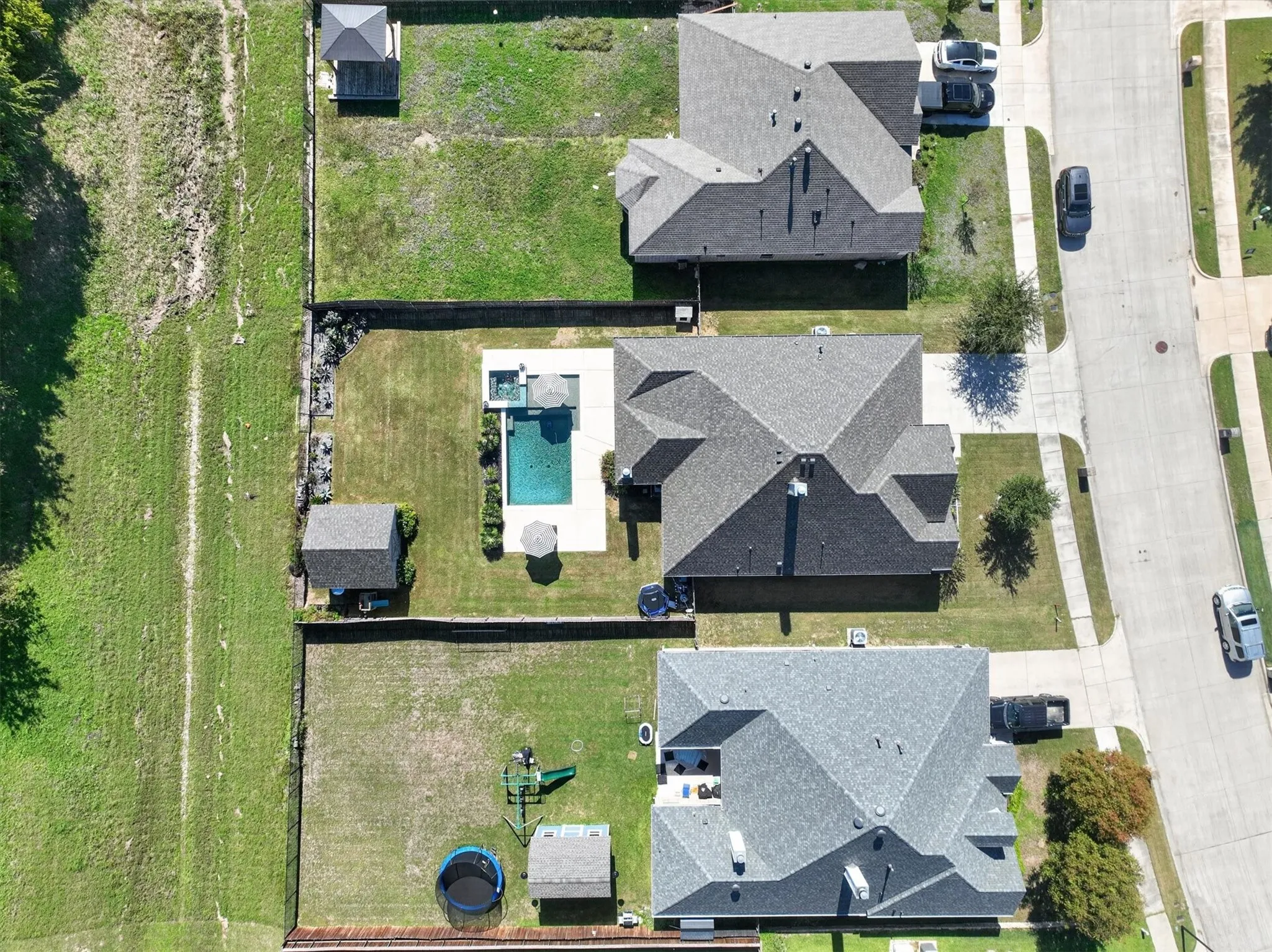 Aerial perspective of a property featuring an in-ground swimming pool, a concrete patio, a dedicated storage structure, and a fenced rear yard