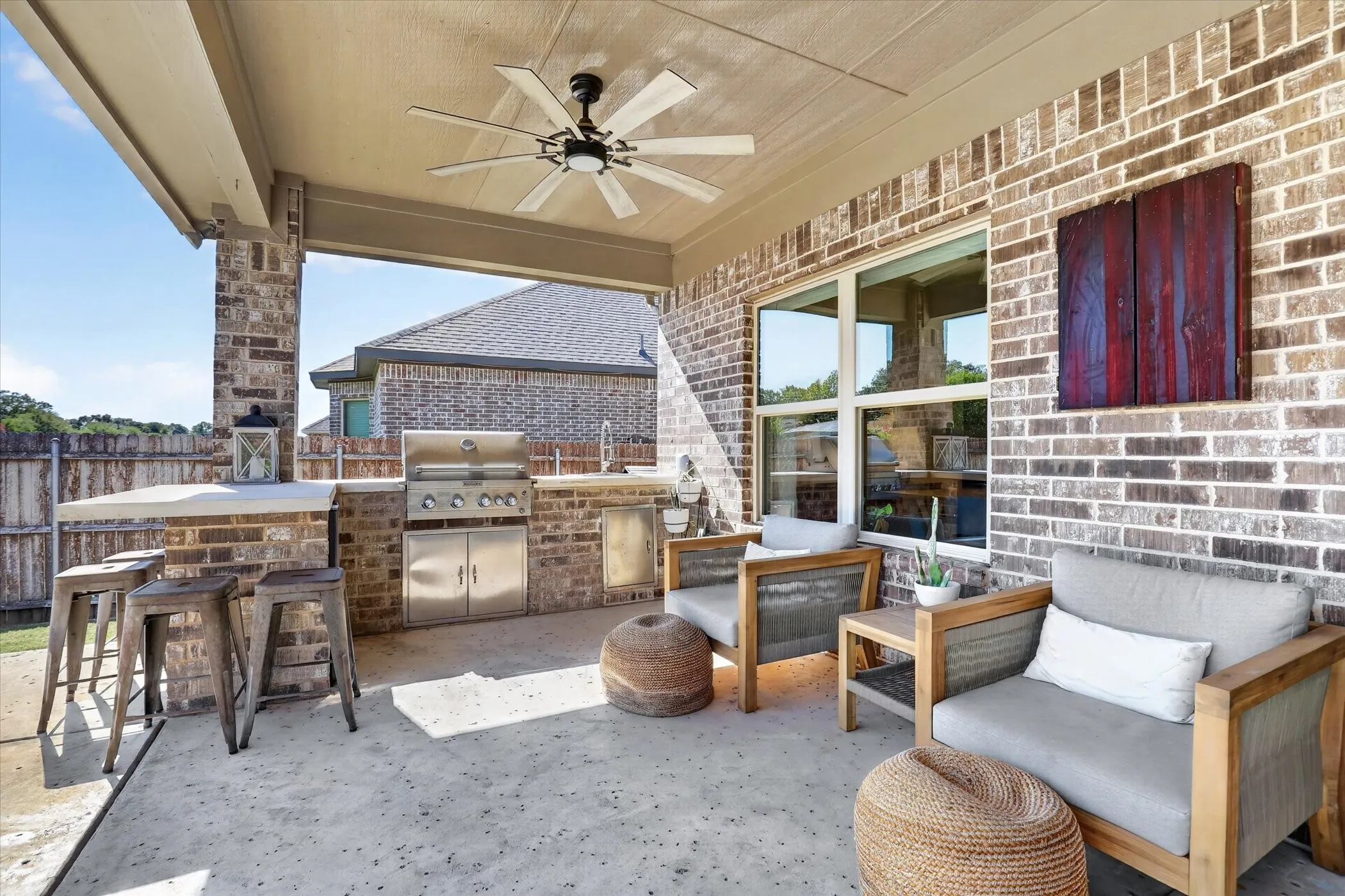 Covered patio featuring a brick exterior, built-in outdoor kitchen with stainless steel appliances, and a ceiling-mounted light fixture with a multi-blade fan