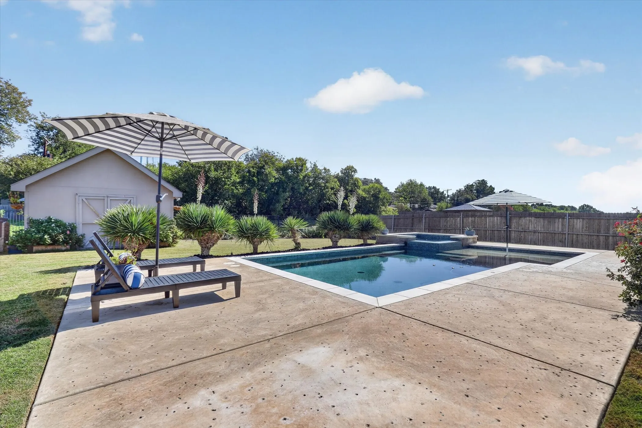 Backyard featuring an in-ground swimming pool with an integrated spa, a concrete pool deck, and a detached structure