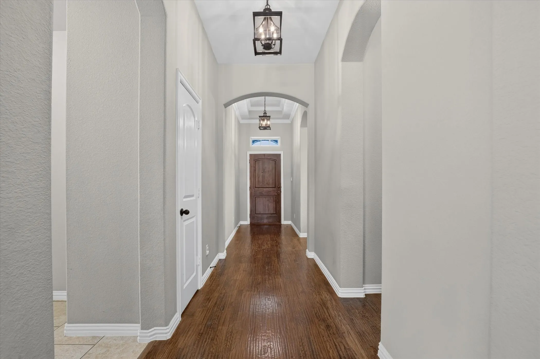Entry hall featuring wood-finish flooring, arched doorways, a coffered ceiling, and two geometric lantern-style pendant light fixtures