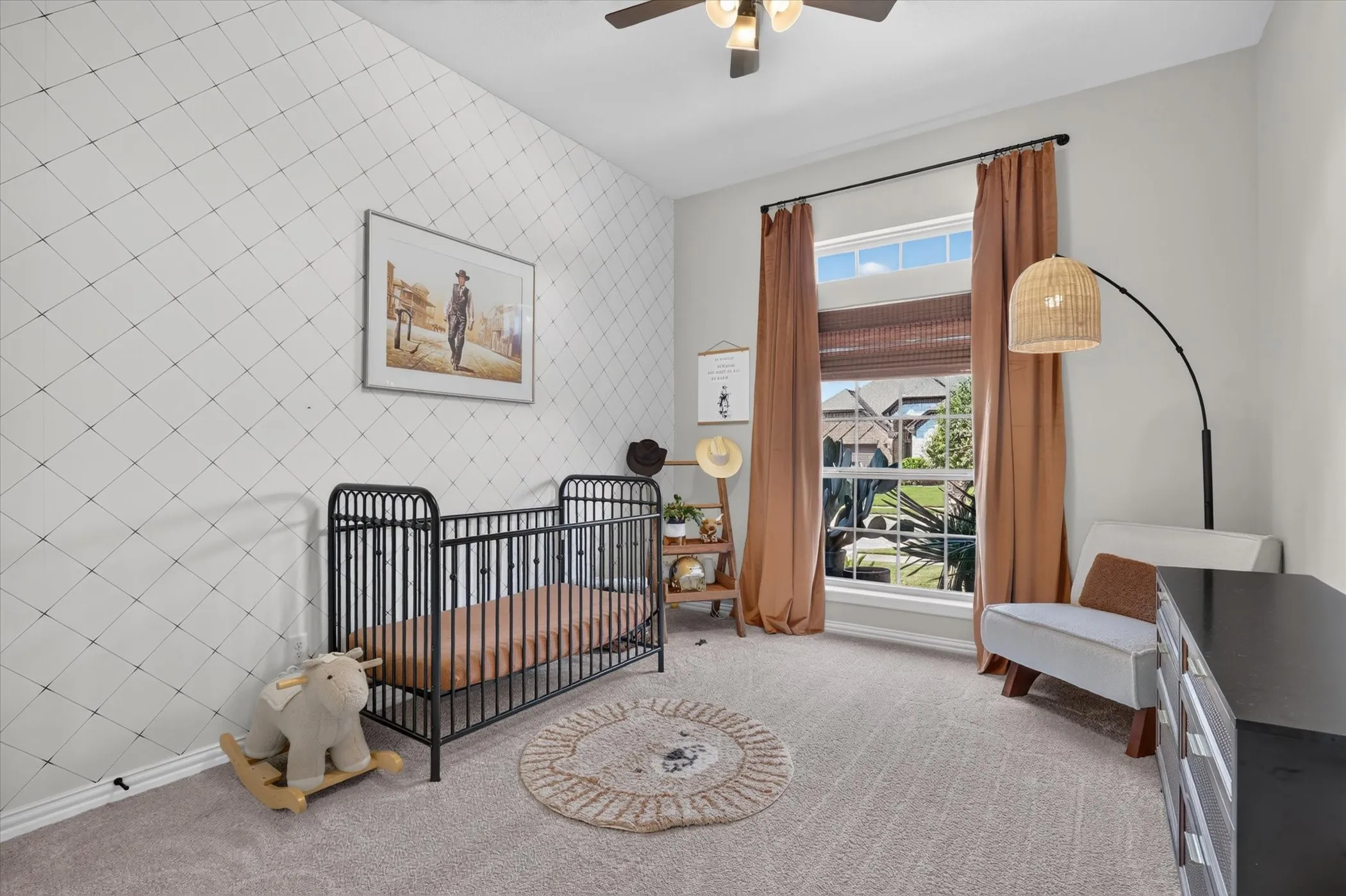 Room featuring a patterned accent wall, neutral carpeting, a transom-style window, and a ceiling fan