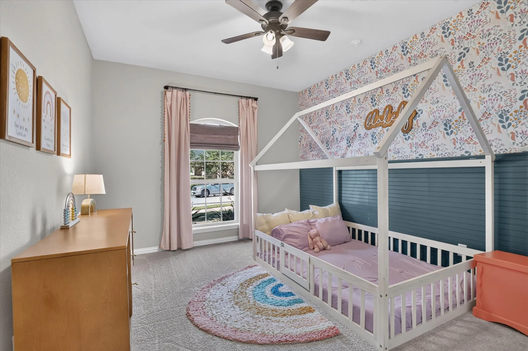 Room featuring an arched window, floral patterned wallpaper accent wall, horizontal slat paneling, wall-to-wall carpeting, and a ceiling fan with integrated lighting