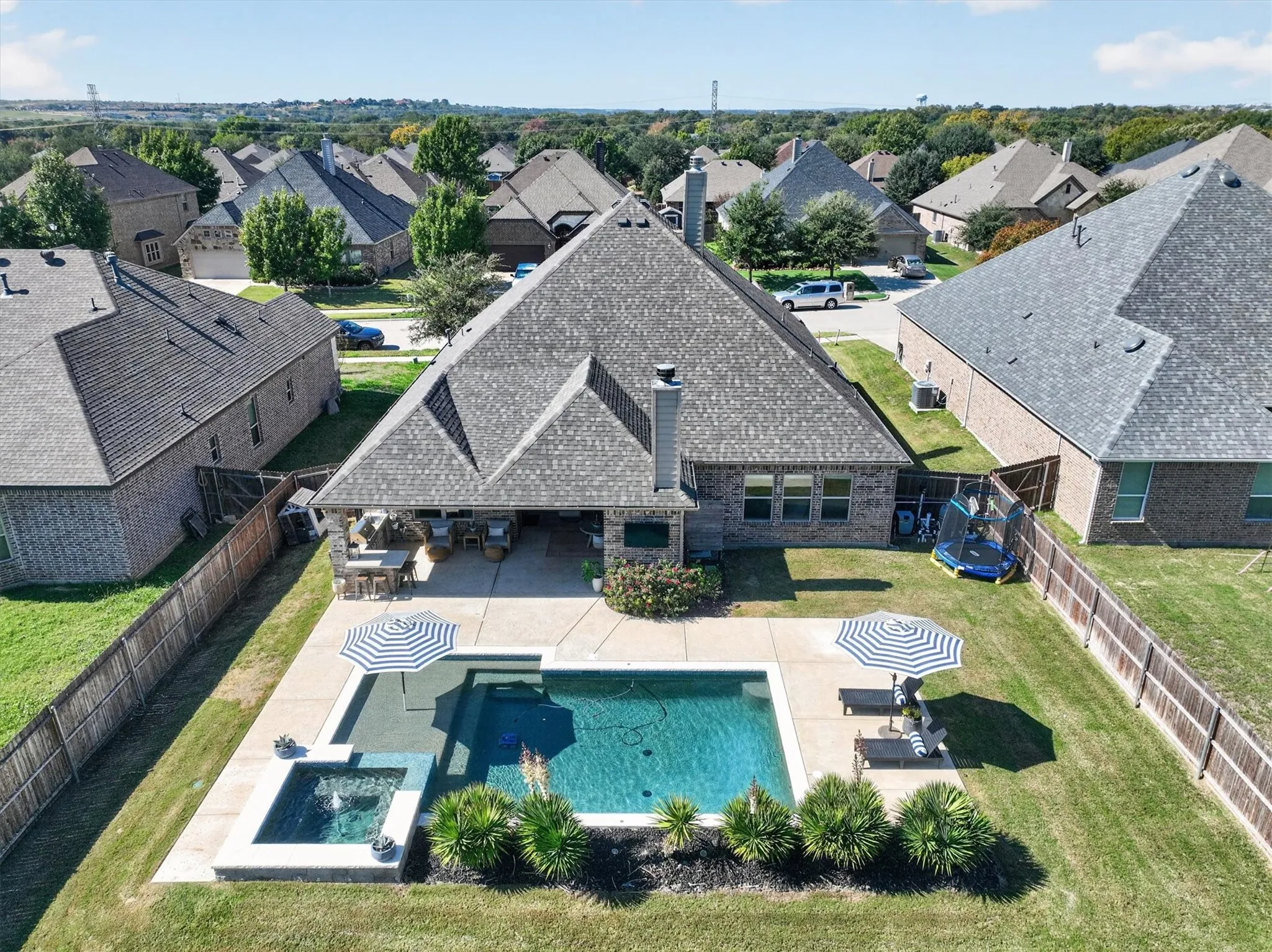 Brick exterior featuring a covered patio, outdoor kitchen, built-in fireplace, and swimming pool with integrated spa