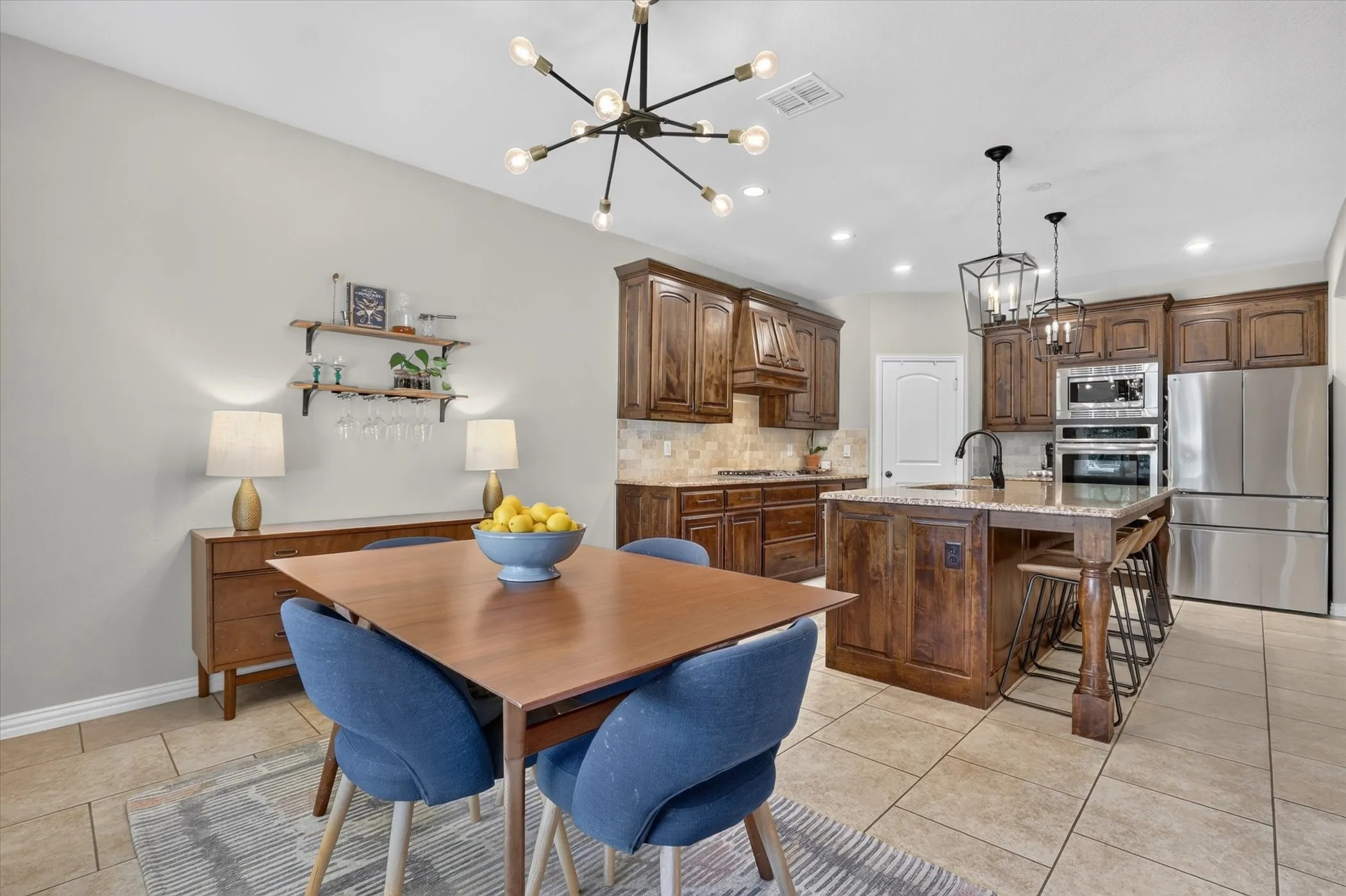 Kitchen featuring stained wood cabinetry, stone tile backsplash, center island with stone countertop, built-in stainless steel double oven, and multi-arm industrial style chandelier