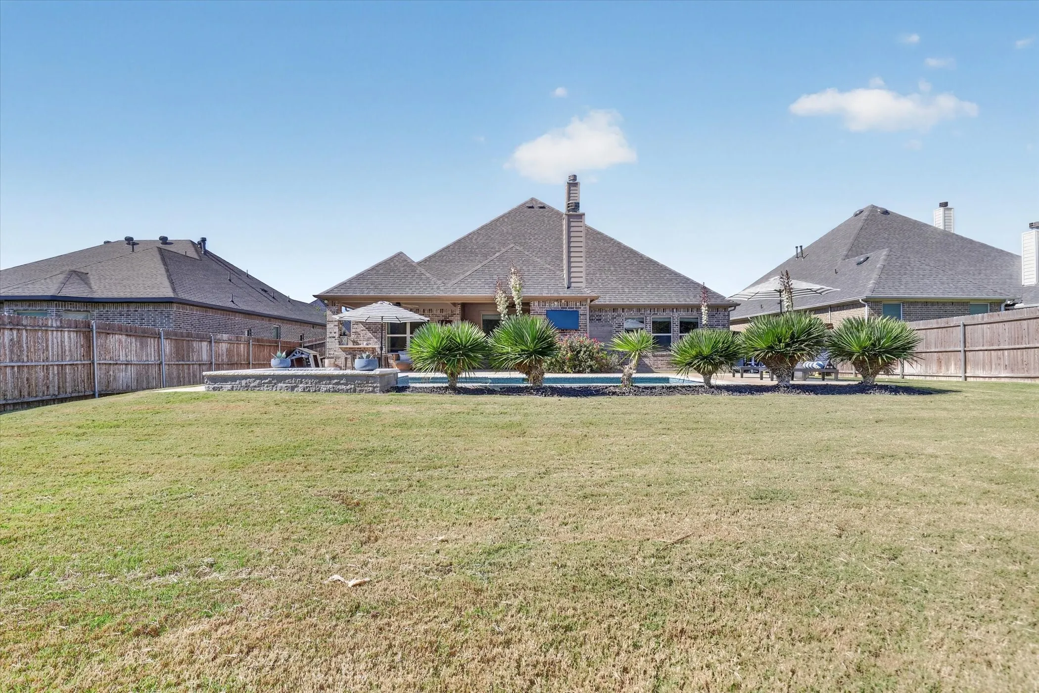 Expansive backyard featuring a built-in swimming pool, stone retaining wall, manicured lawn, and wood privacy fencing