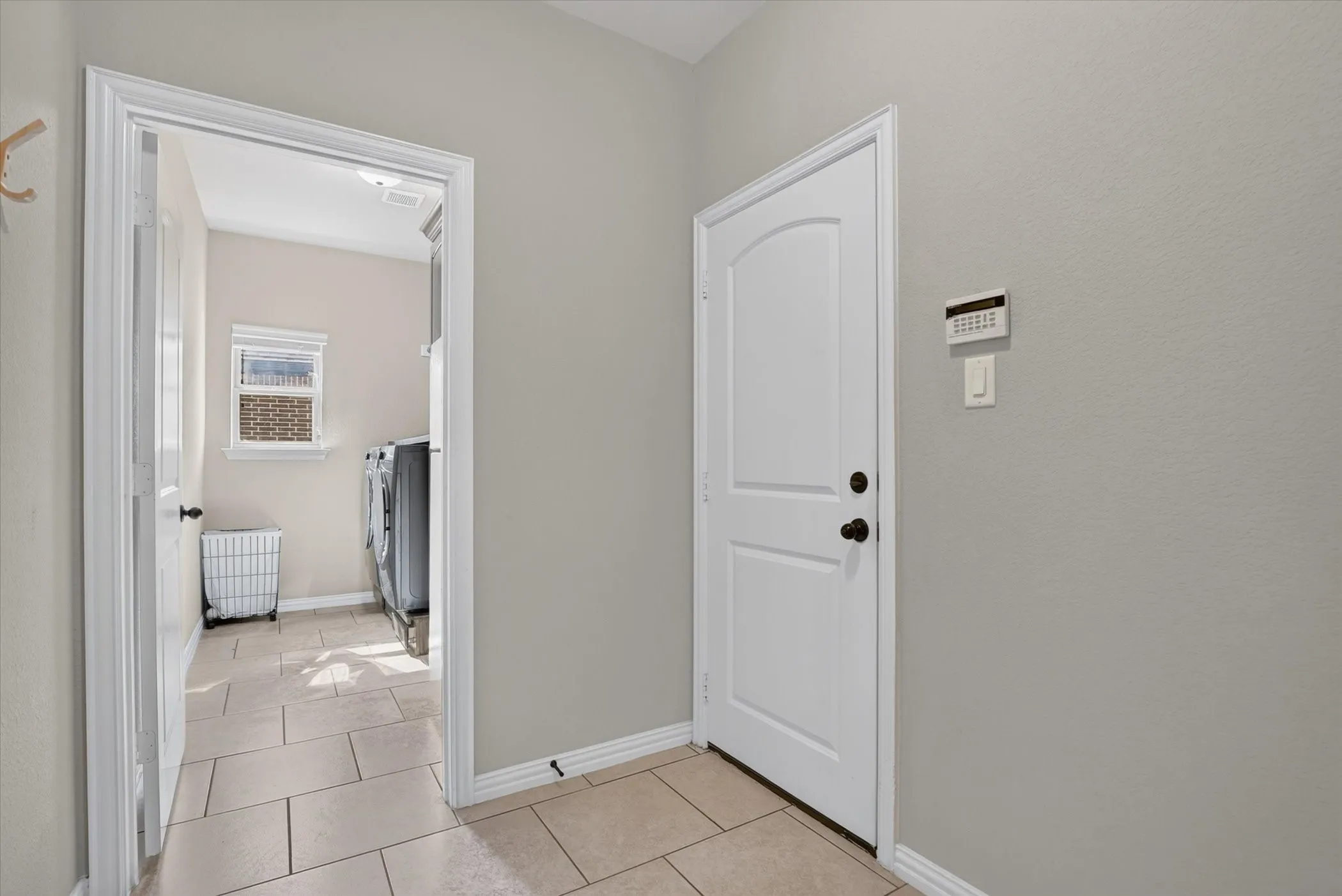 Neutral-toned interior space featuring light-colored tile flooring, an arched-panel entry door, and a dedicated room with a window