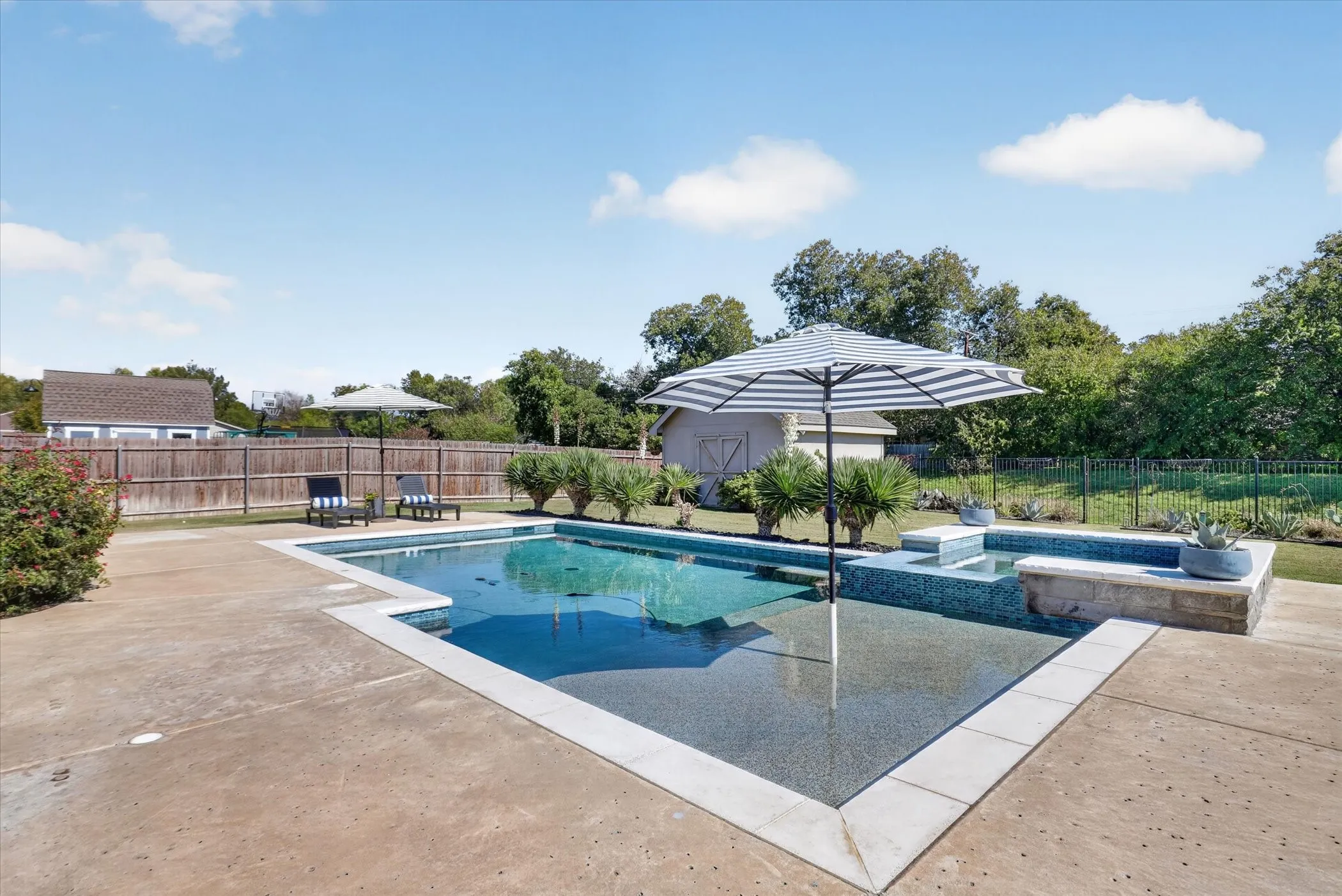 In-ground swimming pool featuring a tanning ledge, raised spillover spa with tile trim, and expansive concrete patio surround