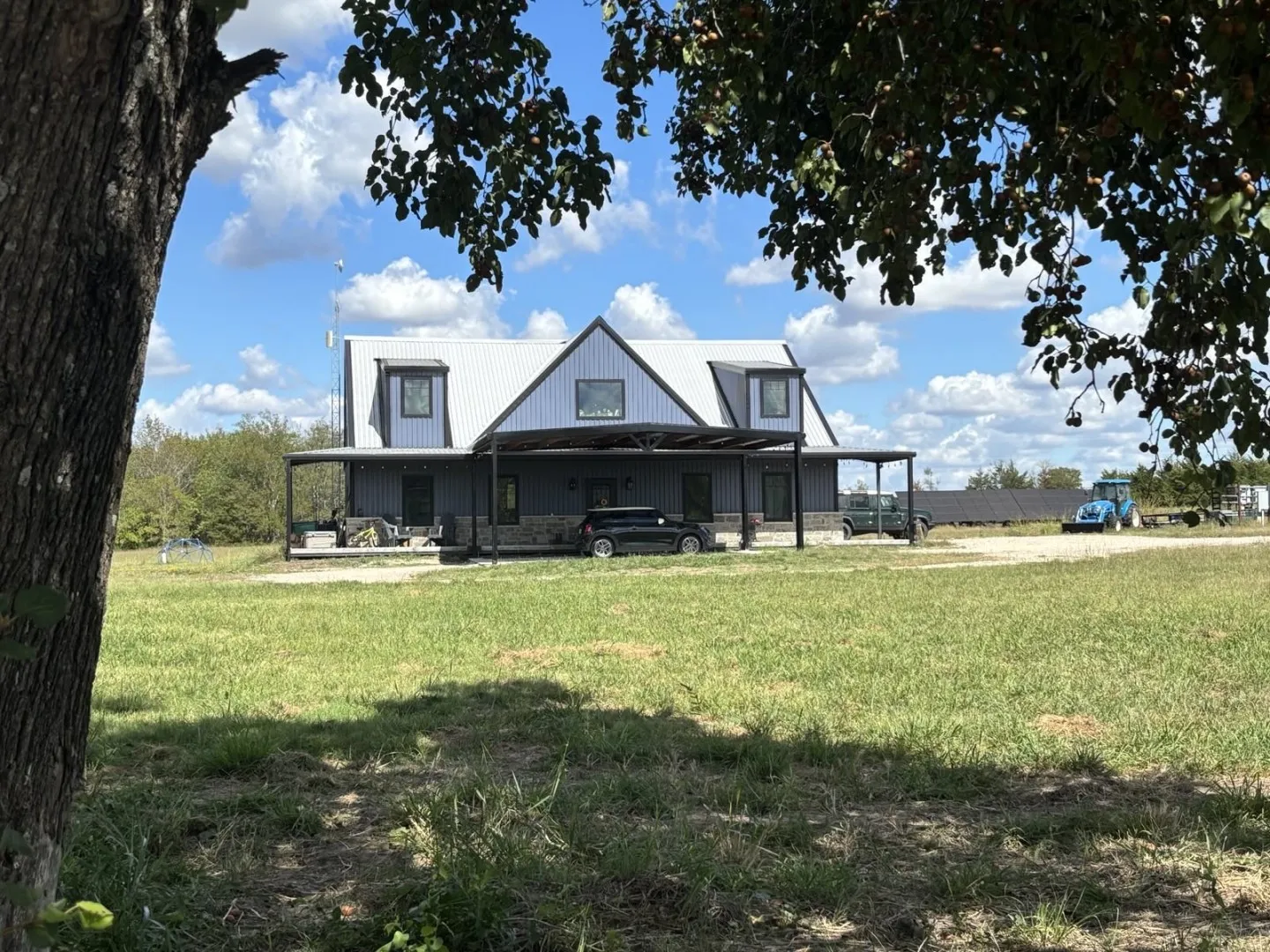 Barndominium-style exterior featuring metal siding, stone veneer accents, a standing seam metal roof, dormer windows, and an expansive covered porch