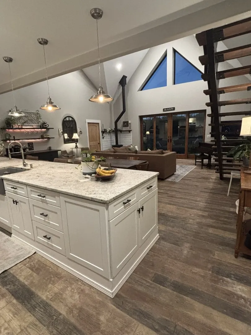 Kitchen island with stone countertop, wood-finish flooring, industrial-style pendant lighting, soaring vaulted ceilings with triangular windows, and open-riser staircase