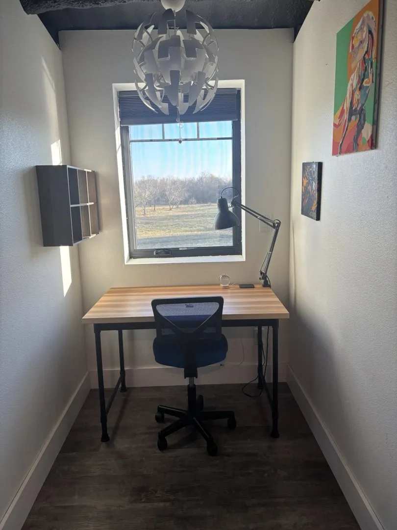 Room featuring wood-finish flooring, a centrally positioned ceiling pendant light, a recessed wall-mounted shelving unit, and a window with exterior landscape exposure