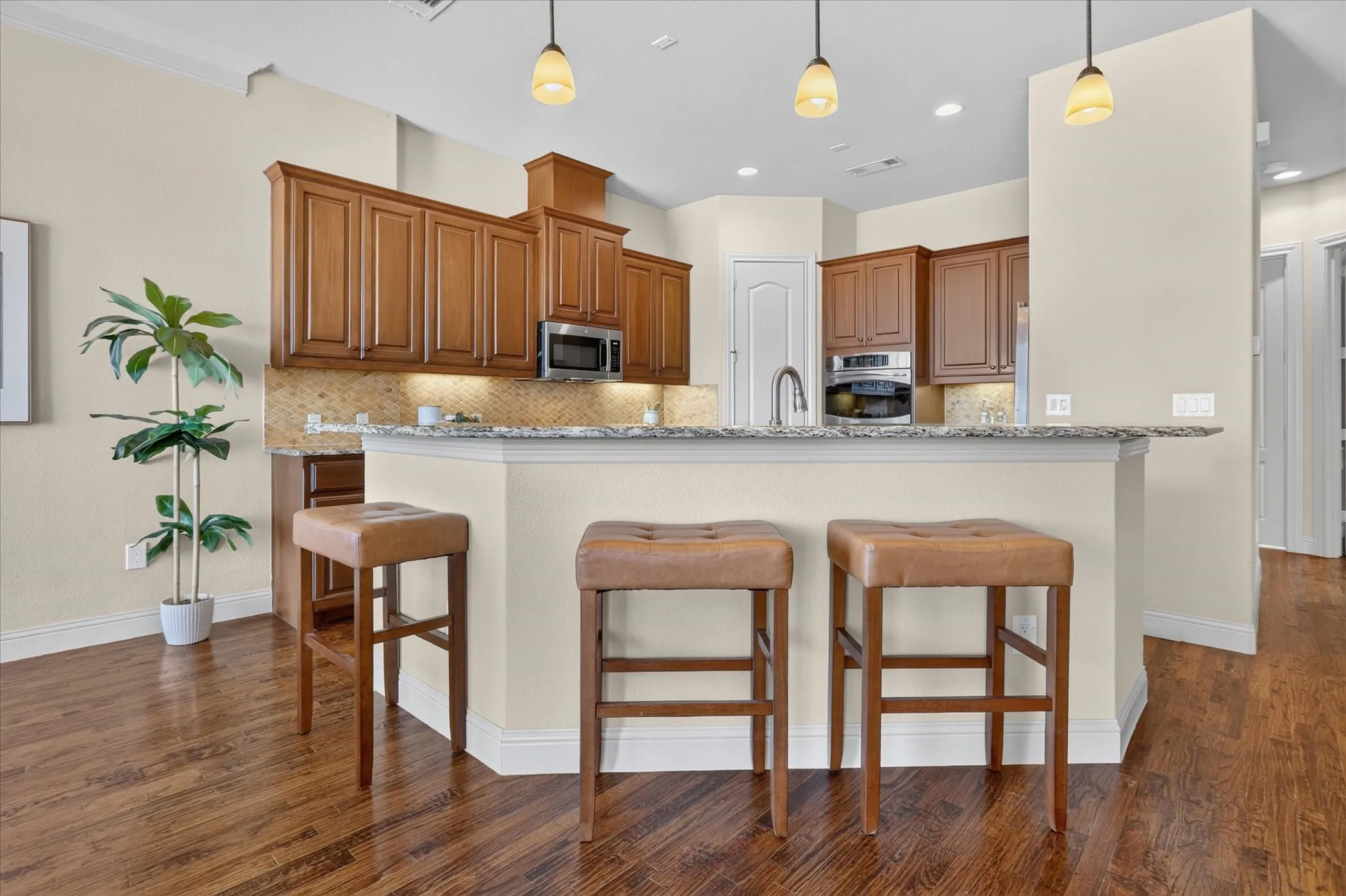 Kitchen featuring wood cabinetry, stone countertops, a breakfast bar, recessed lighting, and stainless steel built-in appliances
