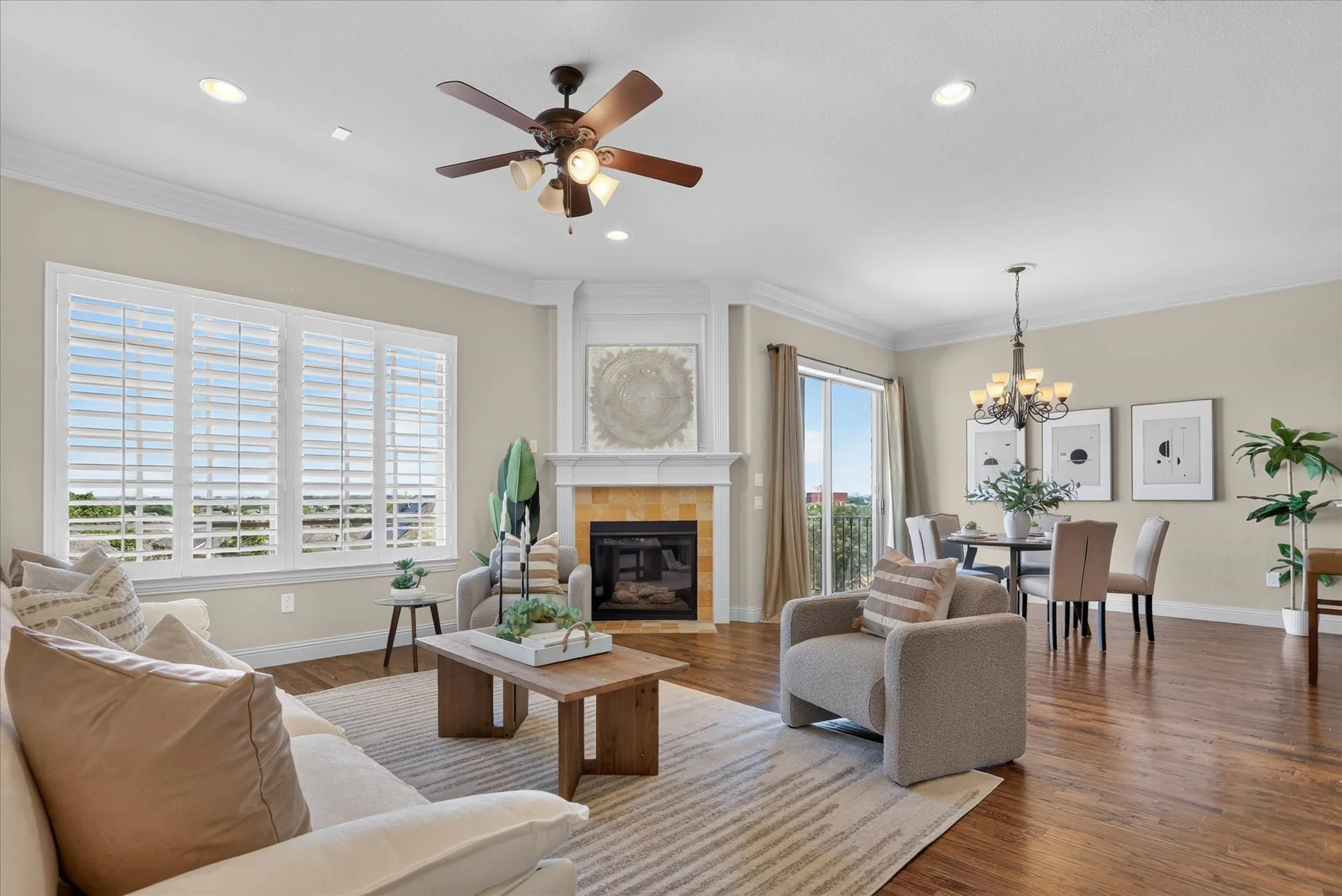 Open-concept area featuring wood-finish flooring, a fireplace with a decorative mantel, plantation shutters, recessed lighting, and crown molding