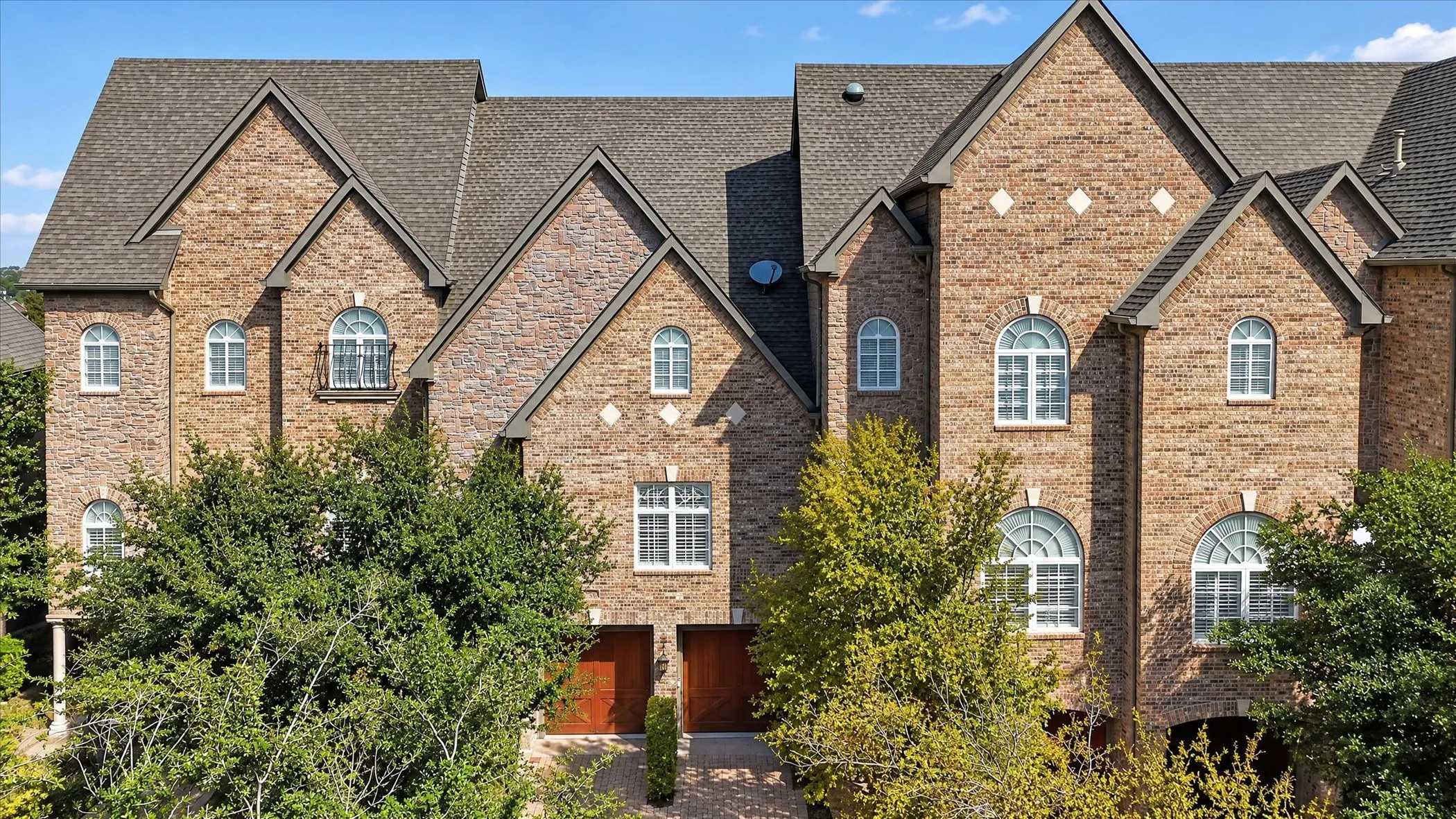 Multi-story brick exterior featuring steep gabled rooflines, arched window detailing, diamond-shaped stone accents, and wood-finish garage doors