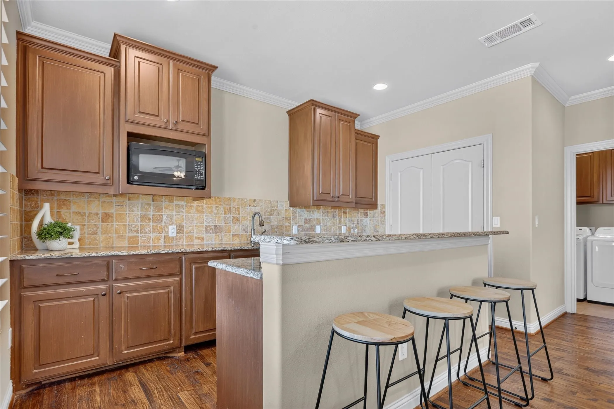 Wet bar kitchen featuring wood cabinetry, granite countertops, square-tile backsplash, built-in microwave, mini sink, and mini fridge. Handscraped wood flooring throughout.