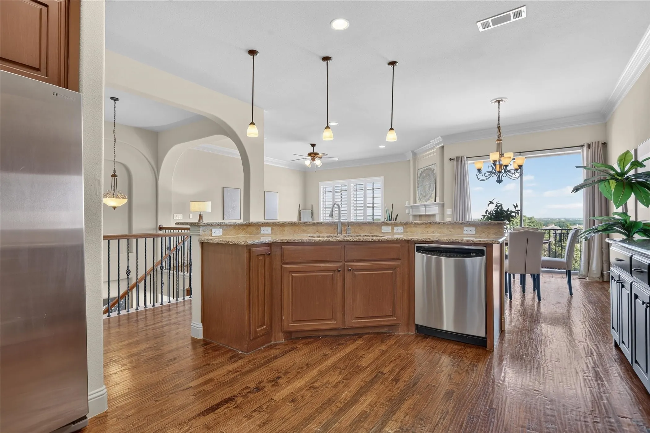 Kitchen featuring wood-finish flooring, a stone-surfaced island with a stainless steel dishwasher, pendant lighting, arched architectural details, and decorative crown molding