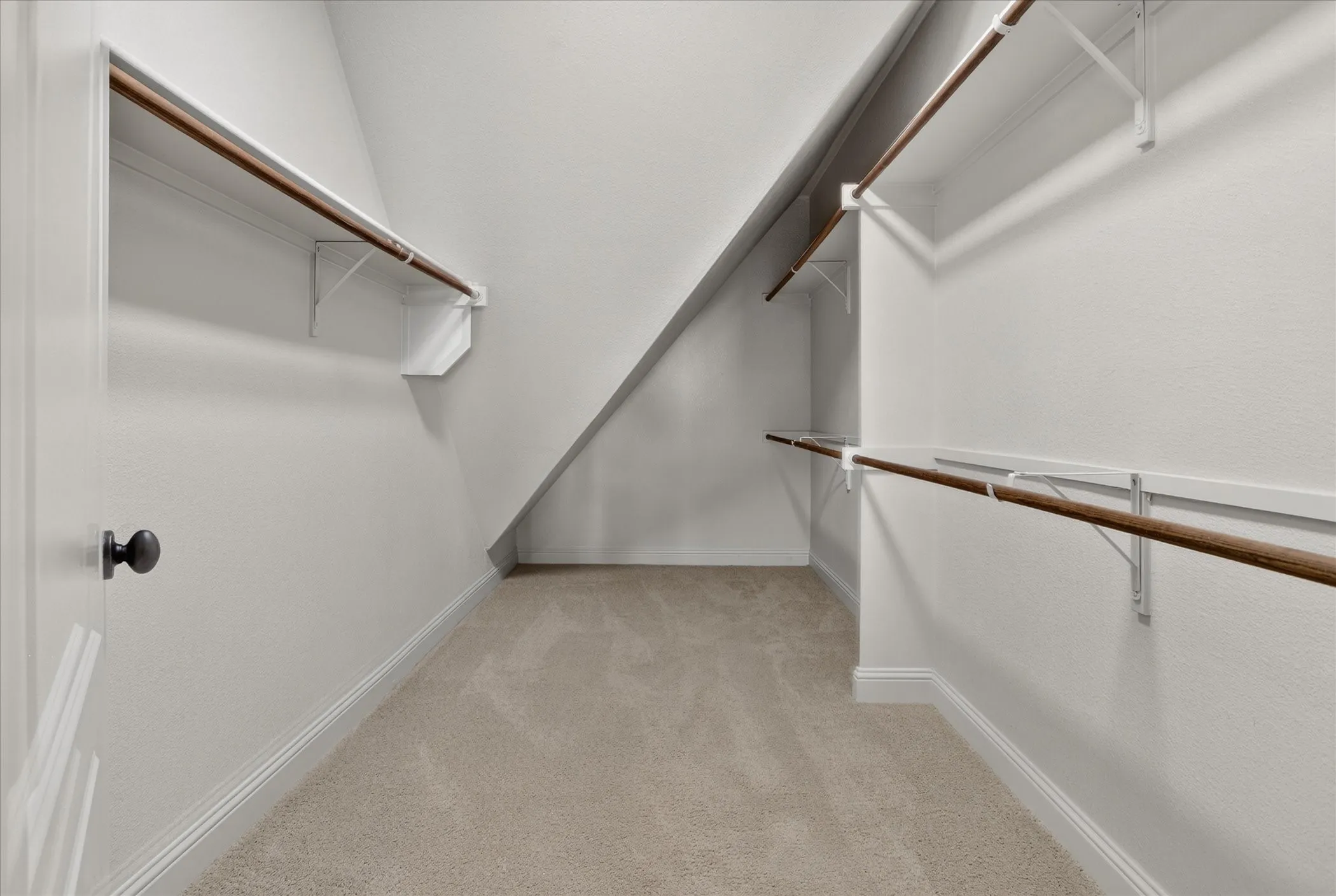 Two of two walk-in closets featuring wall-to-wall carpeting, tiered built-in shelving, and dual-level hanging rods