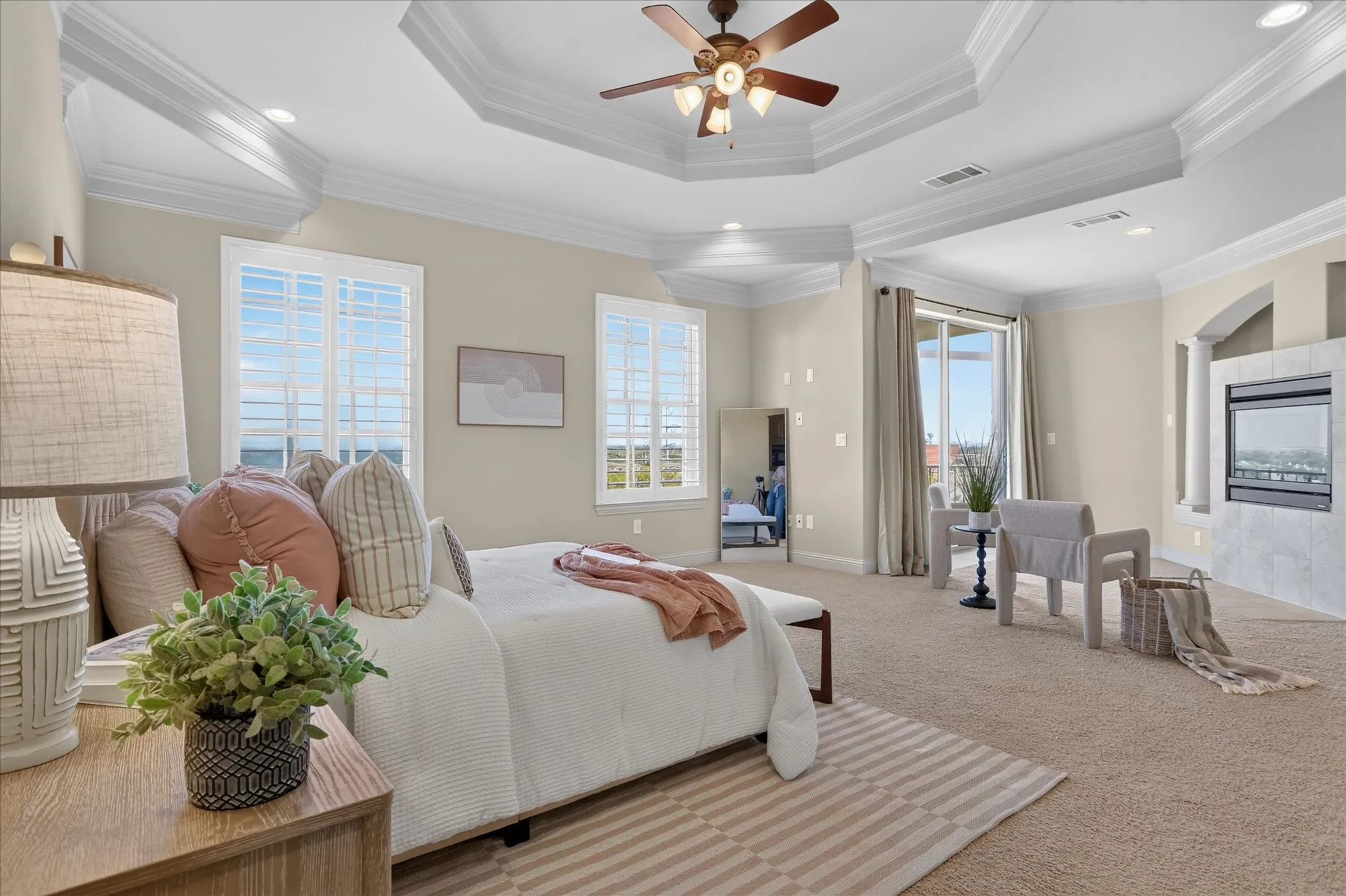 Tray ceiling, recessed lighting, ceiling fan with light kit, plantation shutters, and stone-surround fireplace