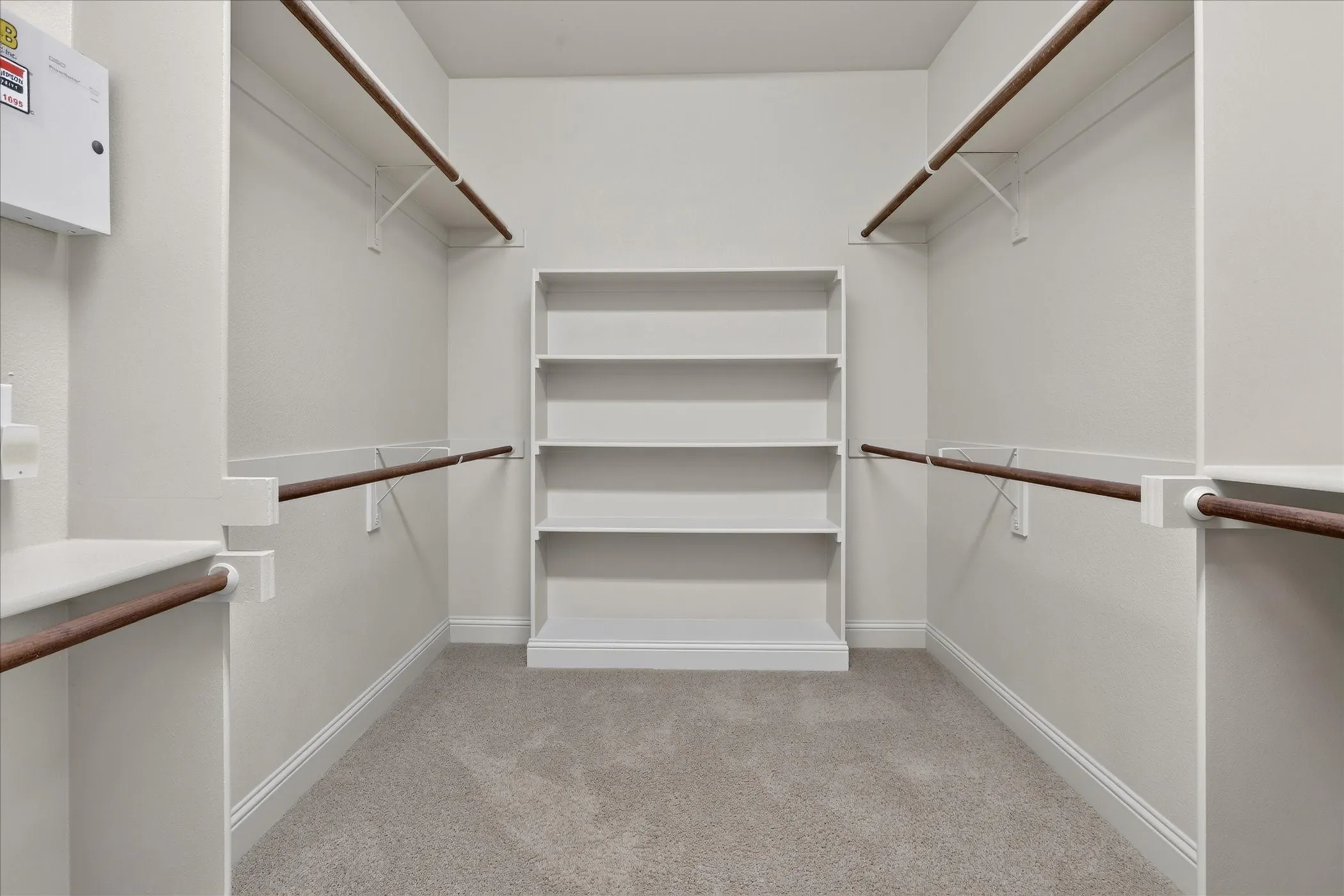One of two walk-in closets featuring wall-to-wall carpeting, tiered built-in shelving, and dual-level hanging rods