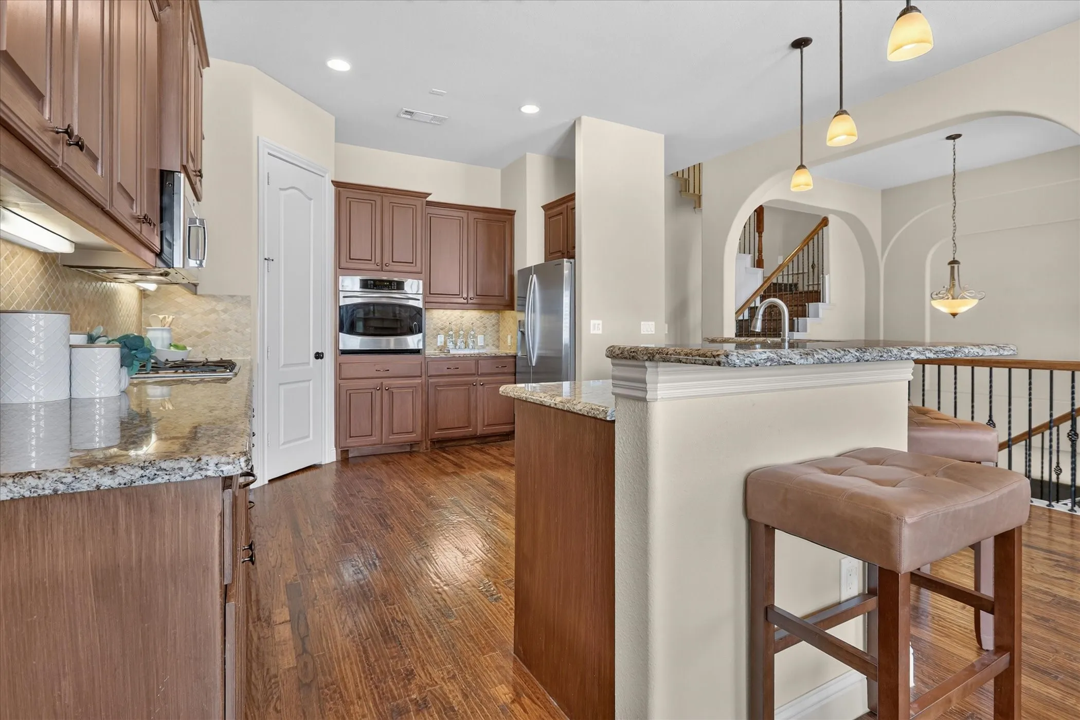 Kitchen featuring wood-finish cabinetry, stone countertops, a stainless steel built-in oven, pendant lighting, and wood-finish flooring