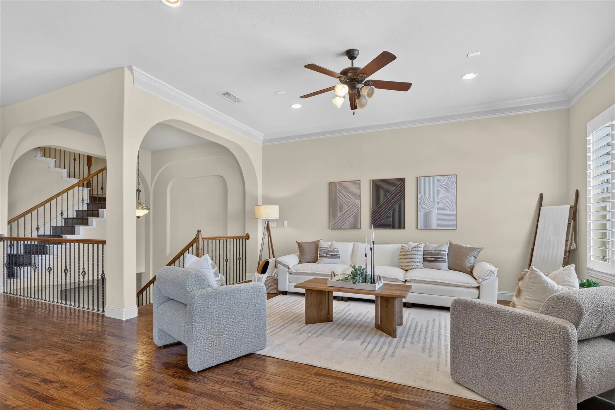 Living area featuring wood-finish flooring, crown molding, arched entryways, recessed lighting, and a ceiling fan with integrated light fixtures