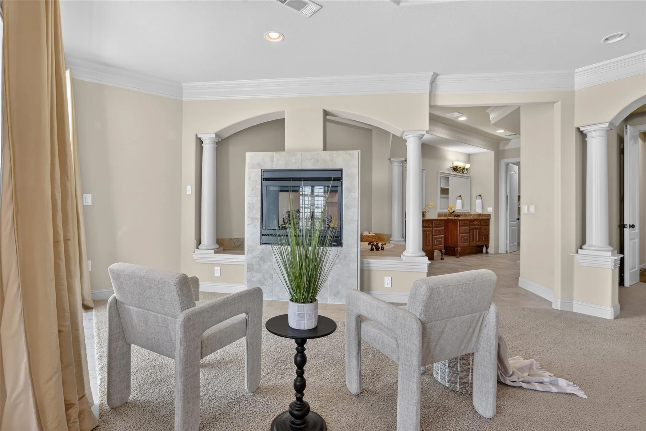 Double-sided fireplace with light-toned stone surround, classical column detailing, crown molding, and recessed lighting
