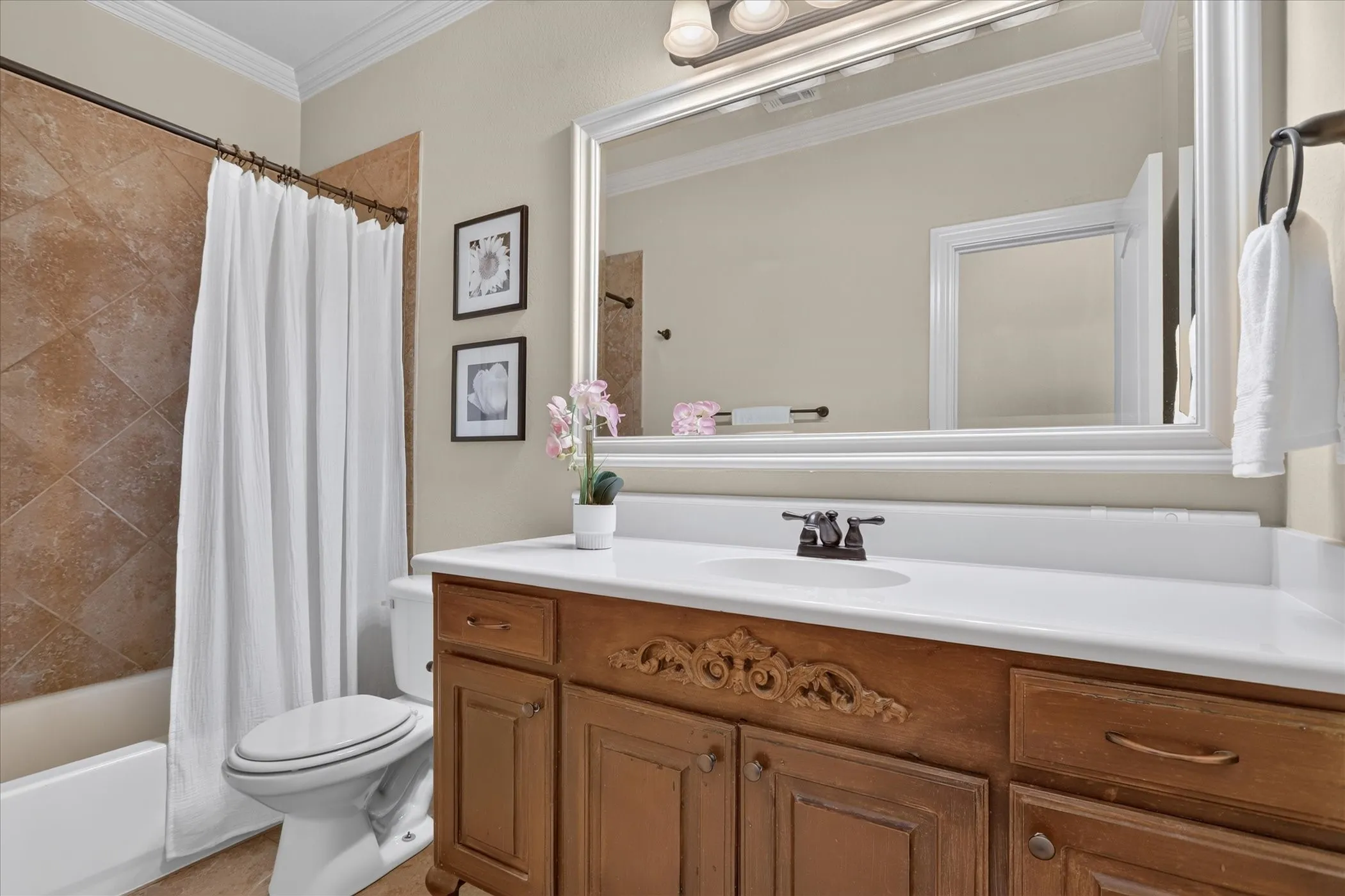 Bathroom featuring a wood vanity with decorative millwork, a white integrated countertop sink, a large framed wall mirror, and a tub enclosure with tile surround