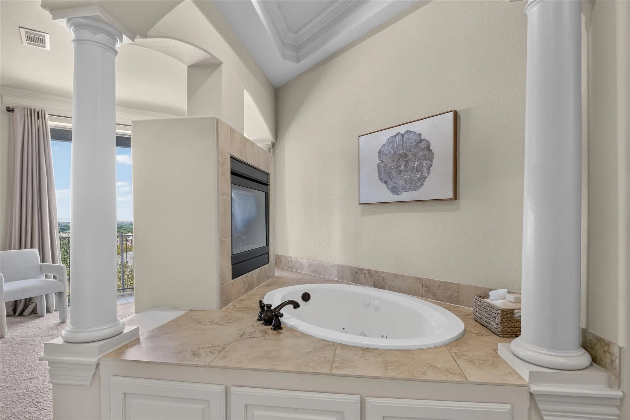Jetted soaking tub with tile surround, dual classical-style columns, and built-in fireplace