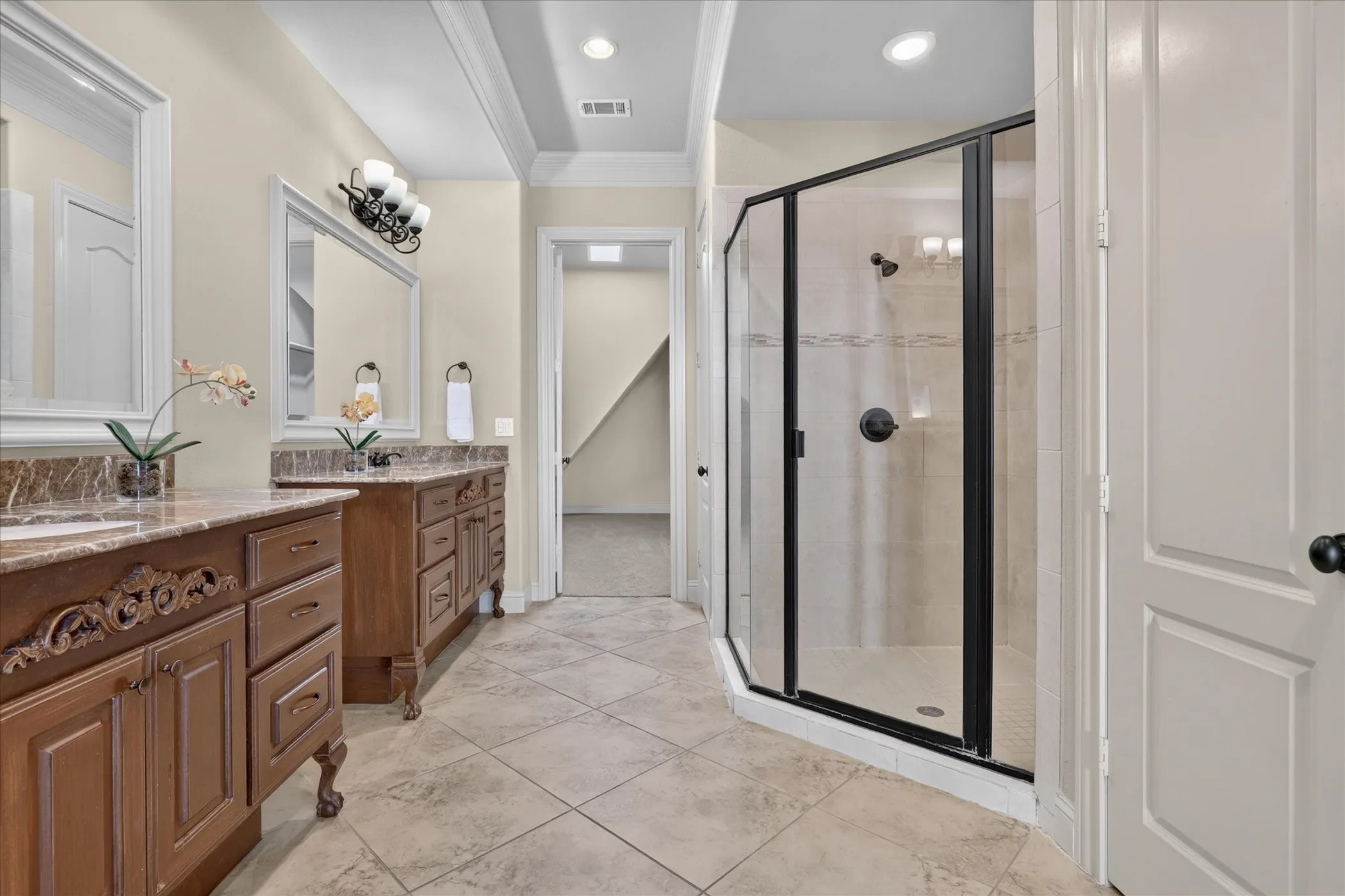 Dual wood cabinetry with stone-finish countertops, ceramic tile flooring, and a walk-in shower featuring a black-framed glass enclosure