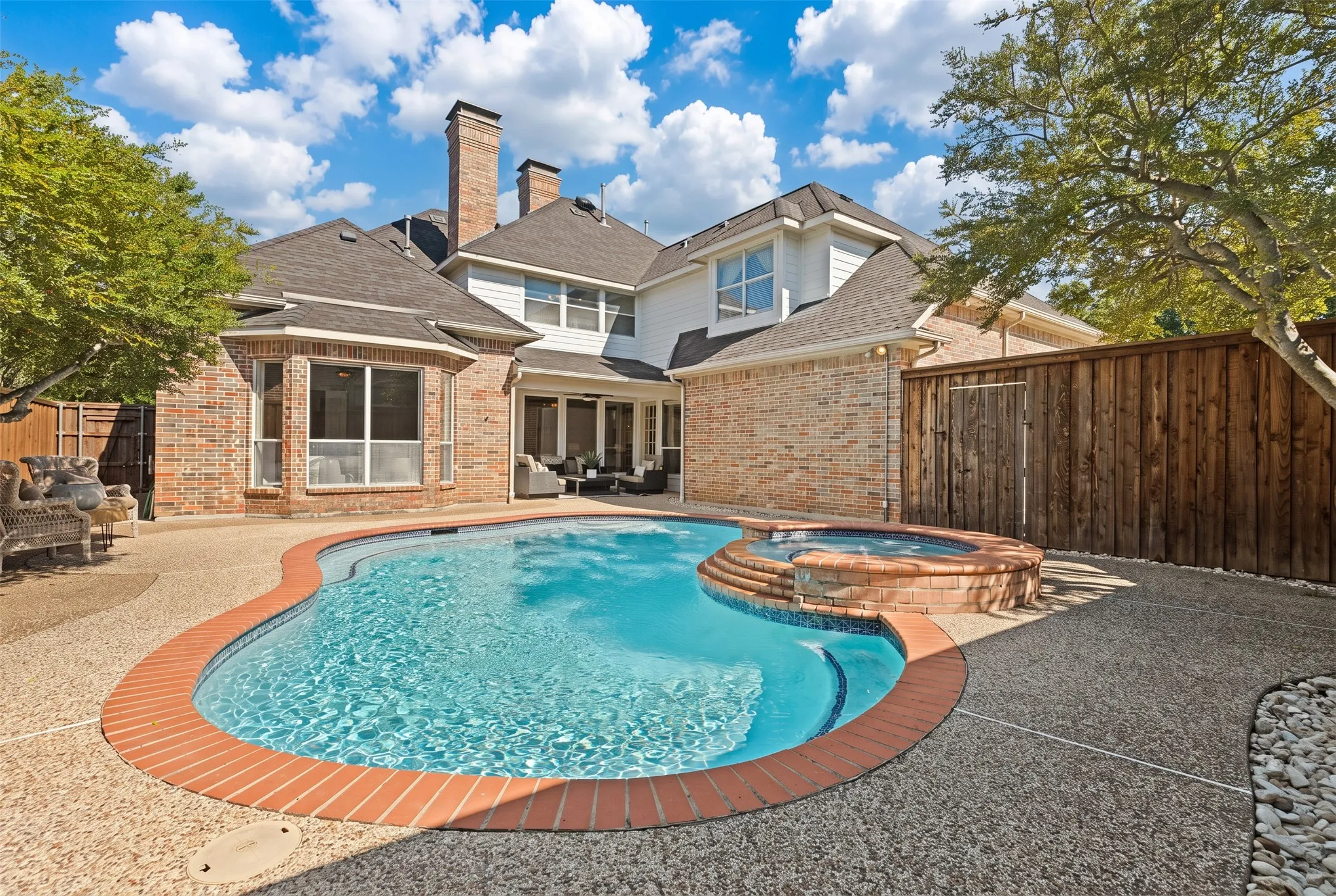 Custom in-ground pool featuring an integrated elevated spa, brick coping, and exposed aggregate concrete patio