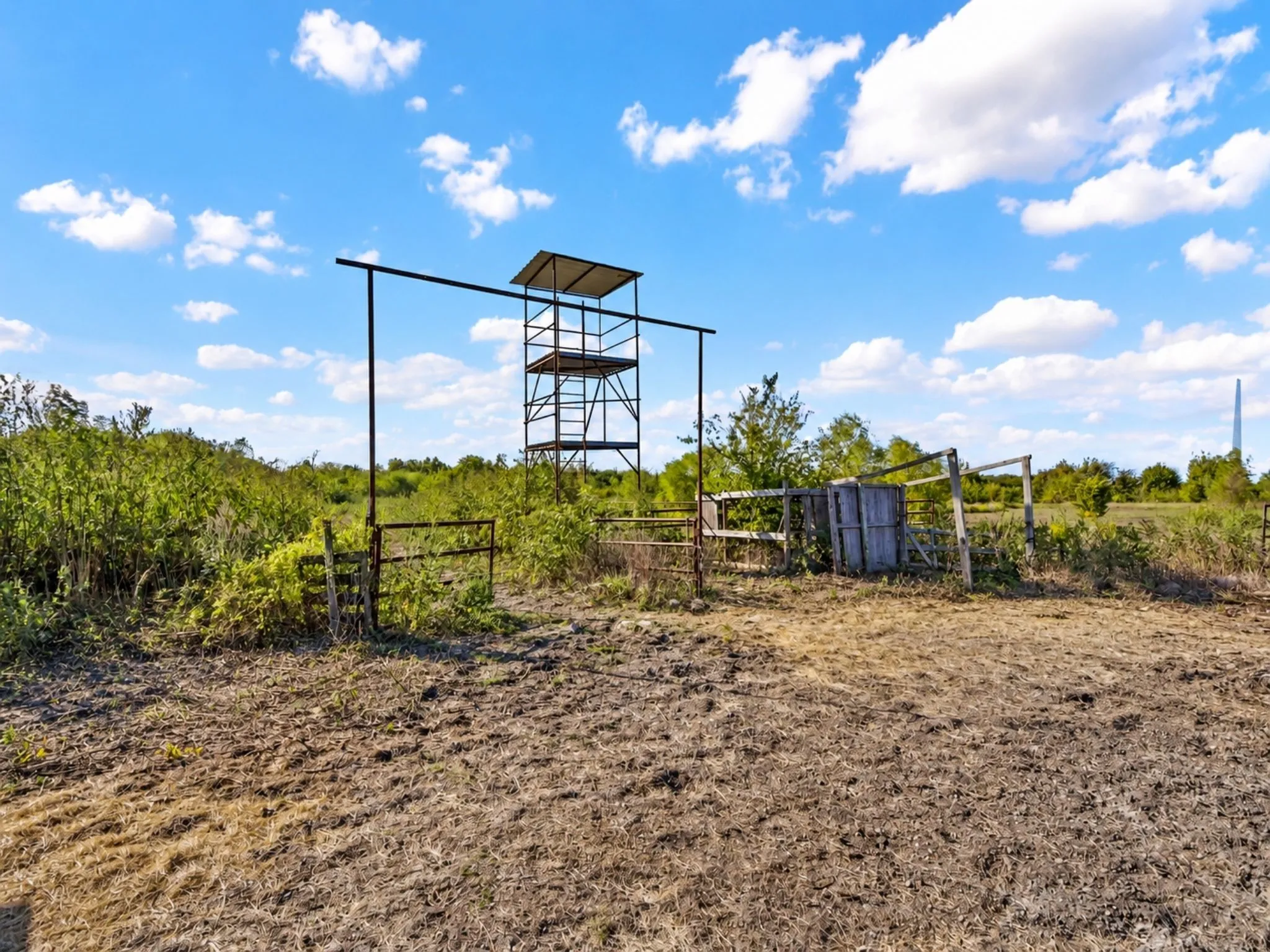 Expansive land featuring a metal observation tower, metal perimeter fencing, and rural vegetation
