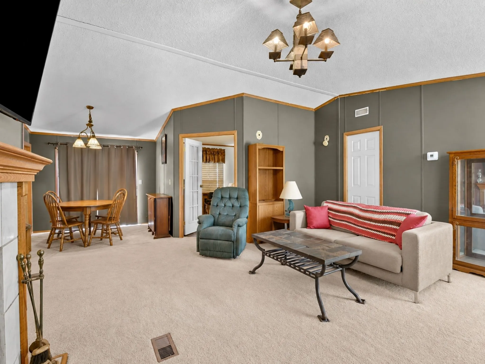 Vaulted ceilings, built-in shelving, a fireplace with a wood mantel, multi-light chandeliers, and French-style interior doors