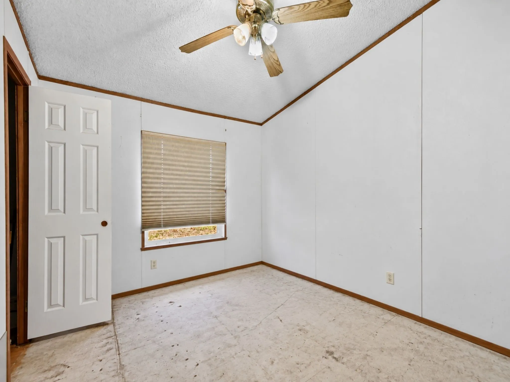 Room interior featuring panelled walls, a six-panel door, a multi-light ceiling fan, and a single window with pleated shades