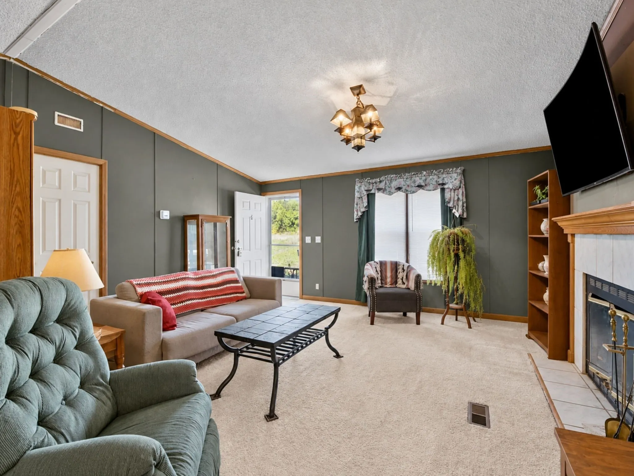 Vaulted ceilings, fireplace with tile surround and wood mantel, built-in shelving, multi-arm light fixture, and neutral carpeting