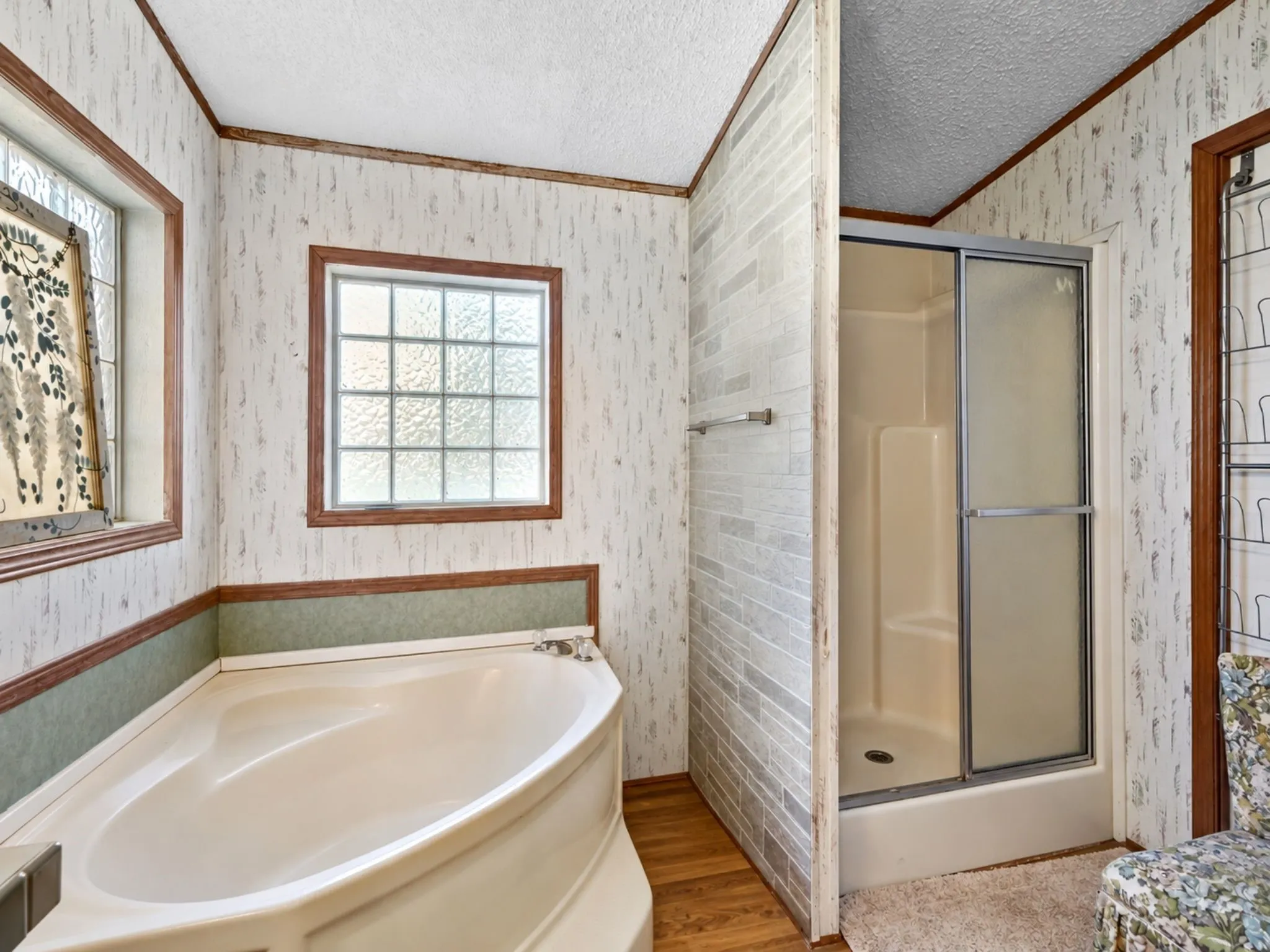 Bathroom featuring a soaking tub, separate shower stall with sliding glass door, grid-patterned windows, and wood-finish flooring
