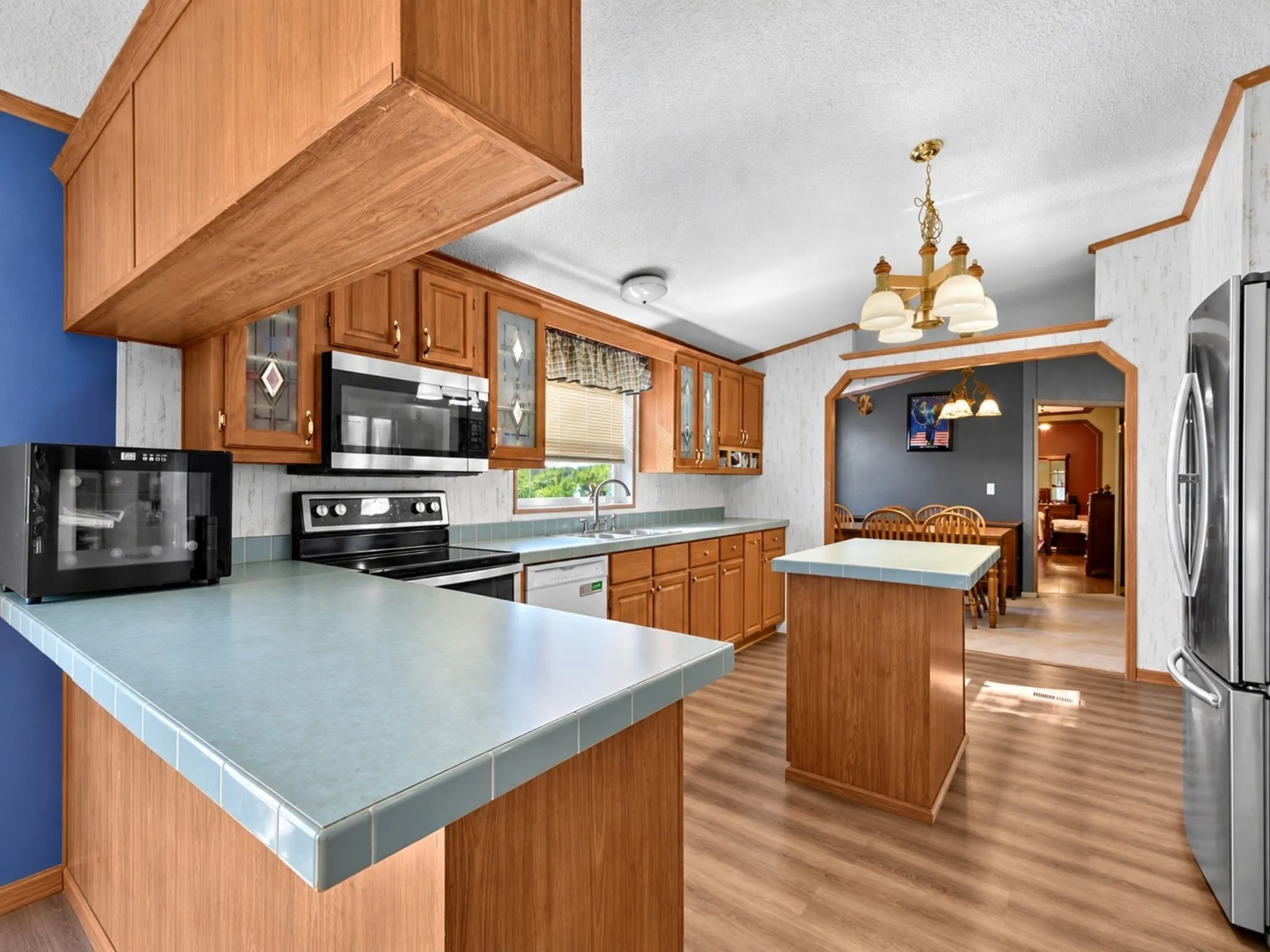 Kitchen featuring wood cabinetry, tiled countertops, stainless steel appliances, a center island, and wood-finish flooring