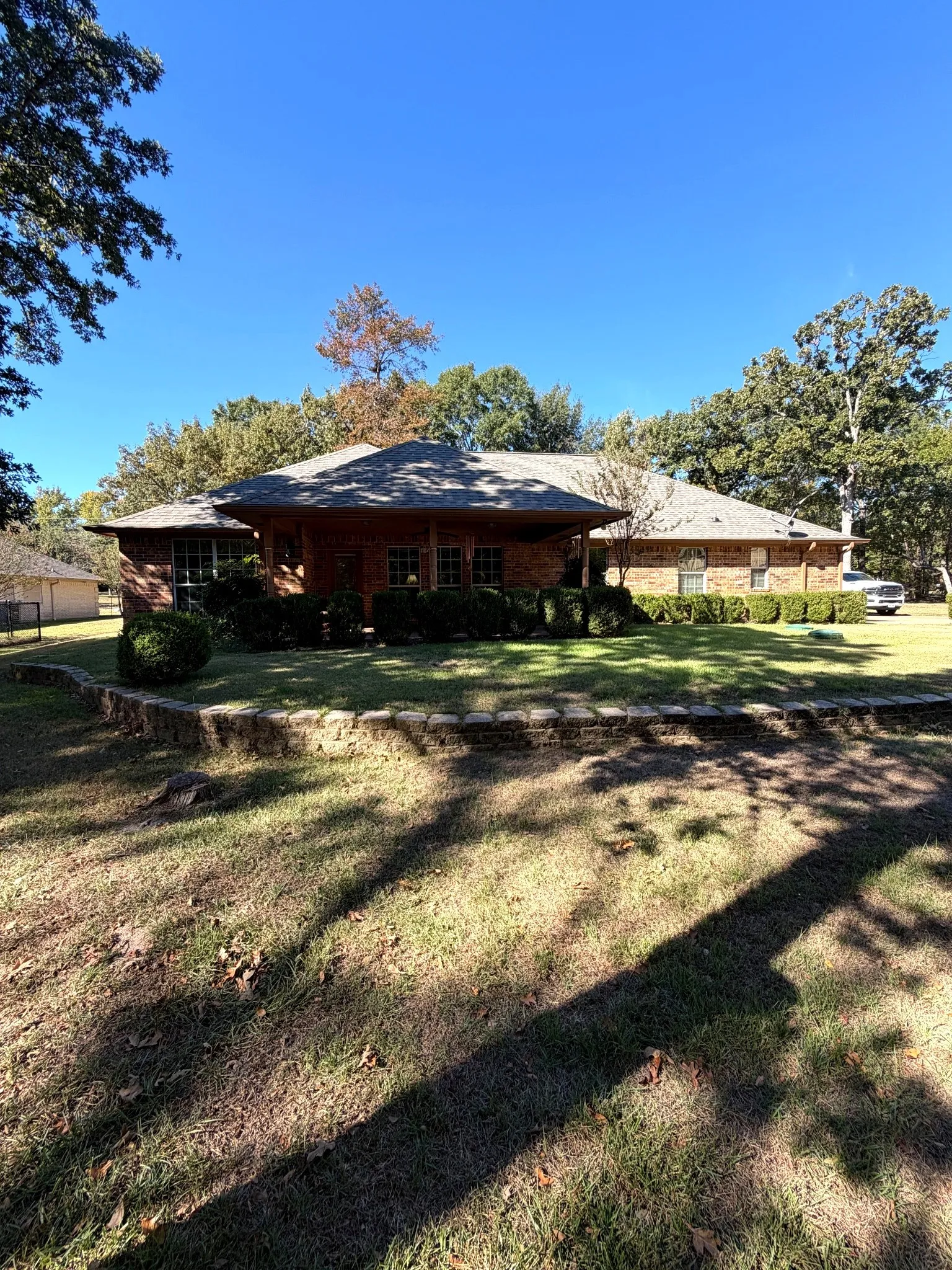 Single-story brick exterior featuring a covered front porch, tiered natural stone retaining wall, and mature landscaping
