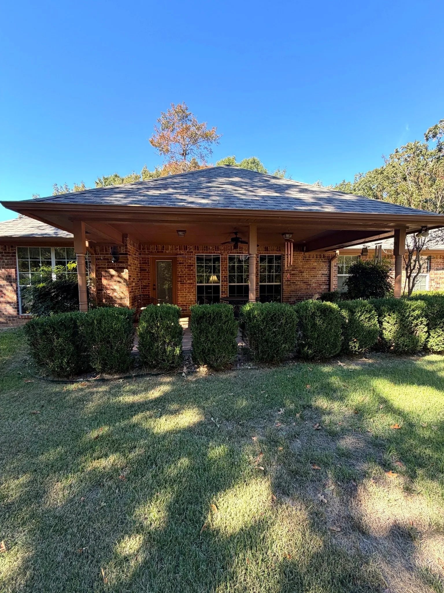 Brick exterior featuring a covered patio, hipped roofline, multiple windows, and a manicured lawn