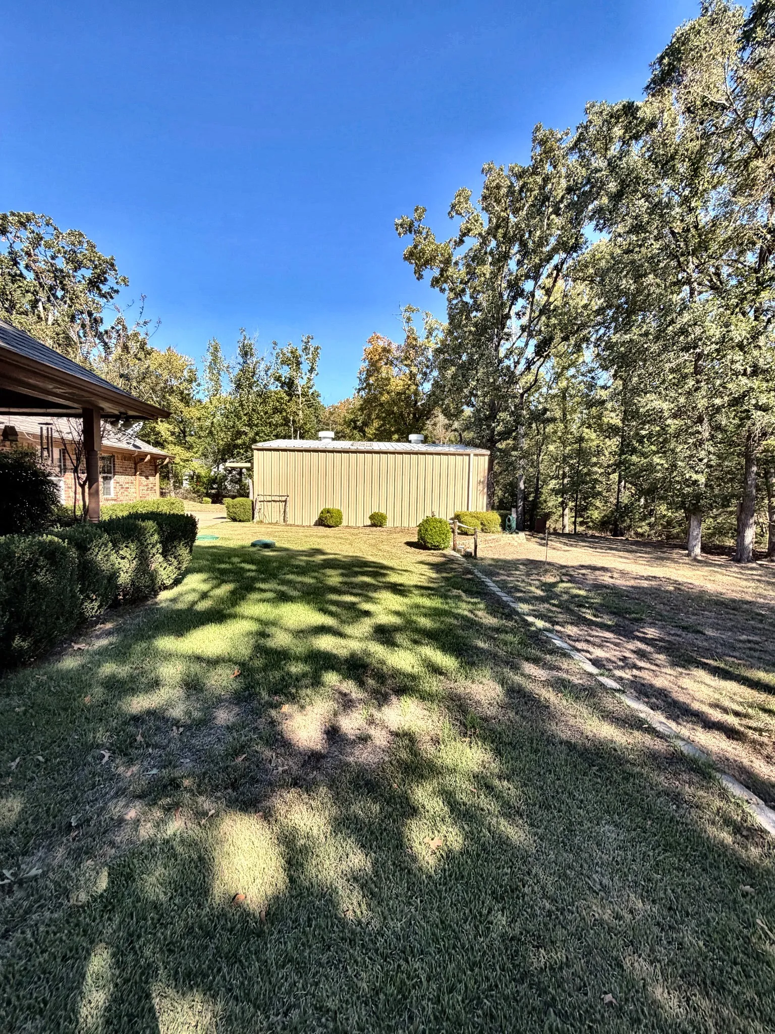Expansive backyard featuring a metal detached structure, mature trees, and landscaping