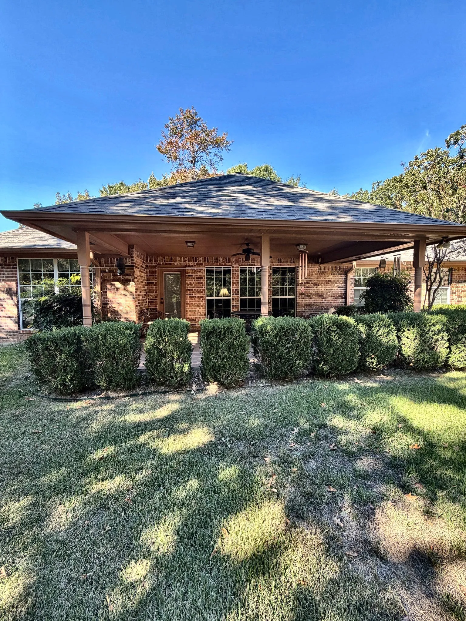 Brick exterior featuring a covered patio, hipped roofline, and mature landscaping