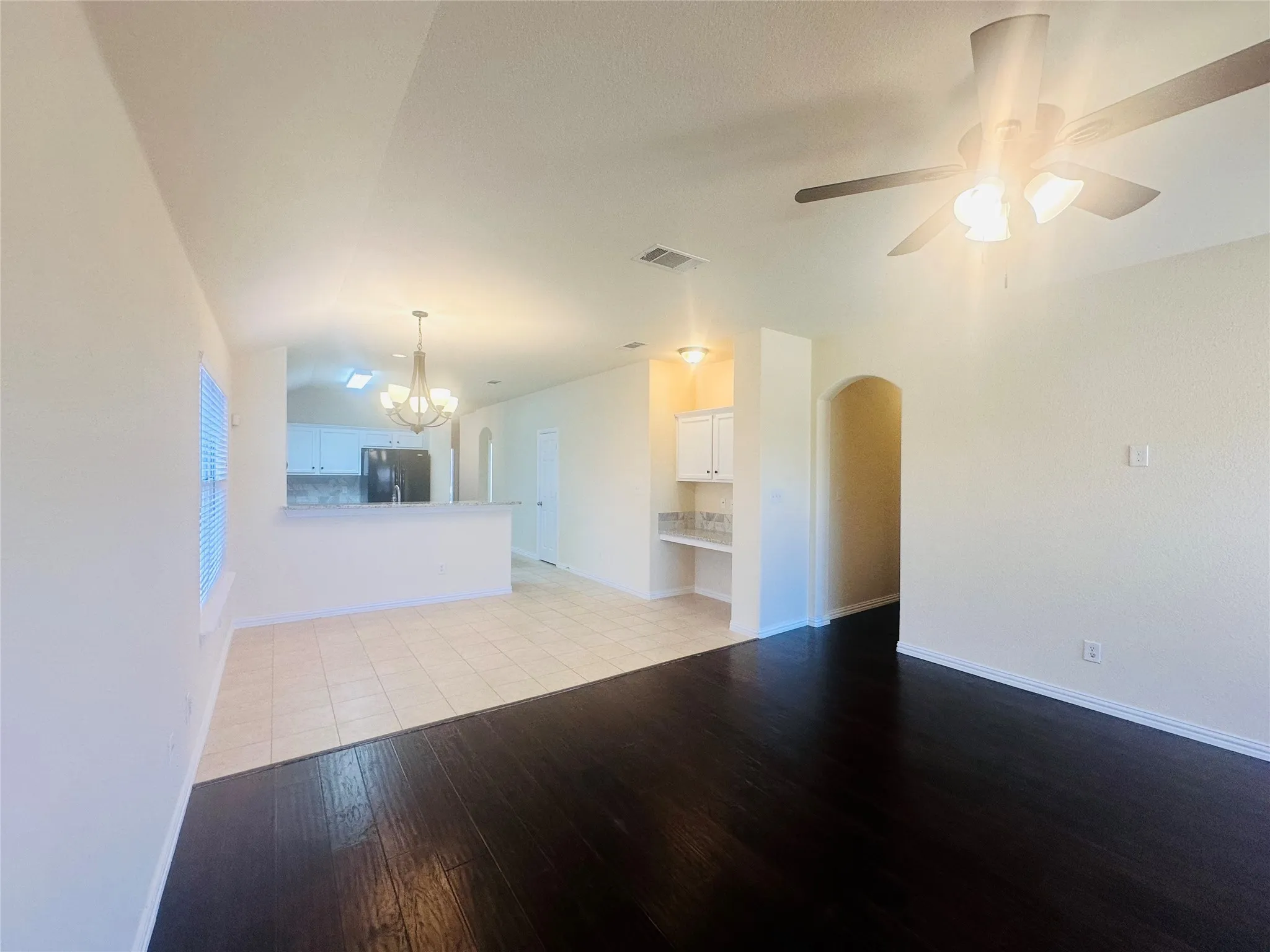 Unfurnished living room with lofted ceiling, ceiling fan with notable chandelier, and light hardwood / wood-style floors