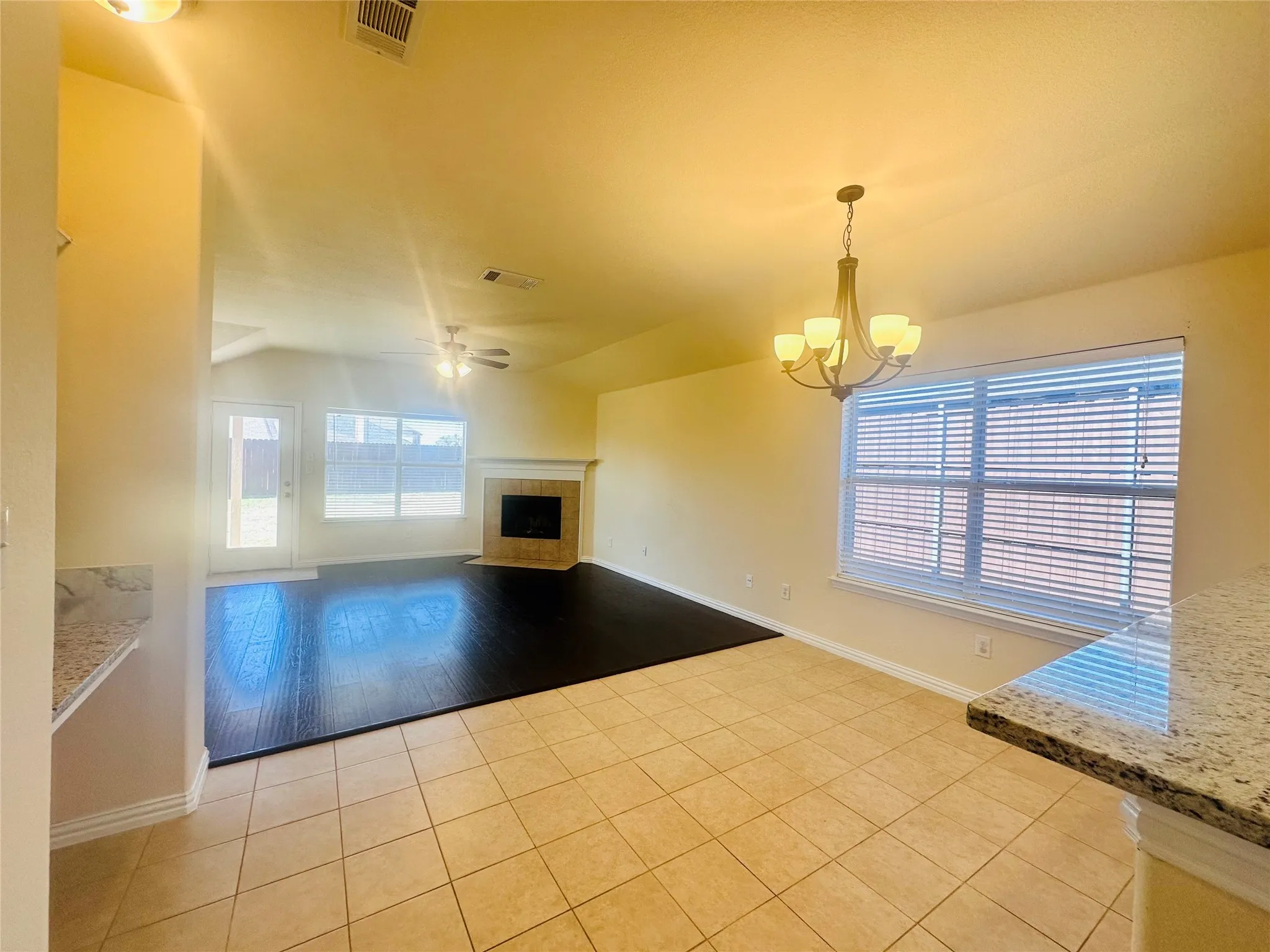 Unfurnished living room with a tiled fireplace, ceiling fan with notable chandelier, lofted ceiling, and light tile patterned flooring