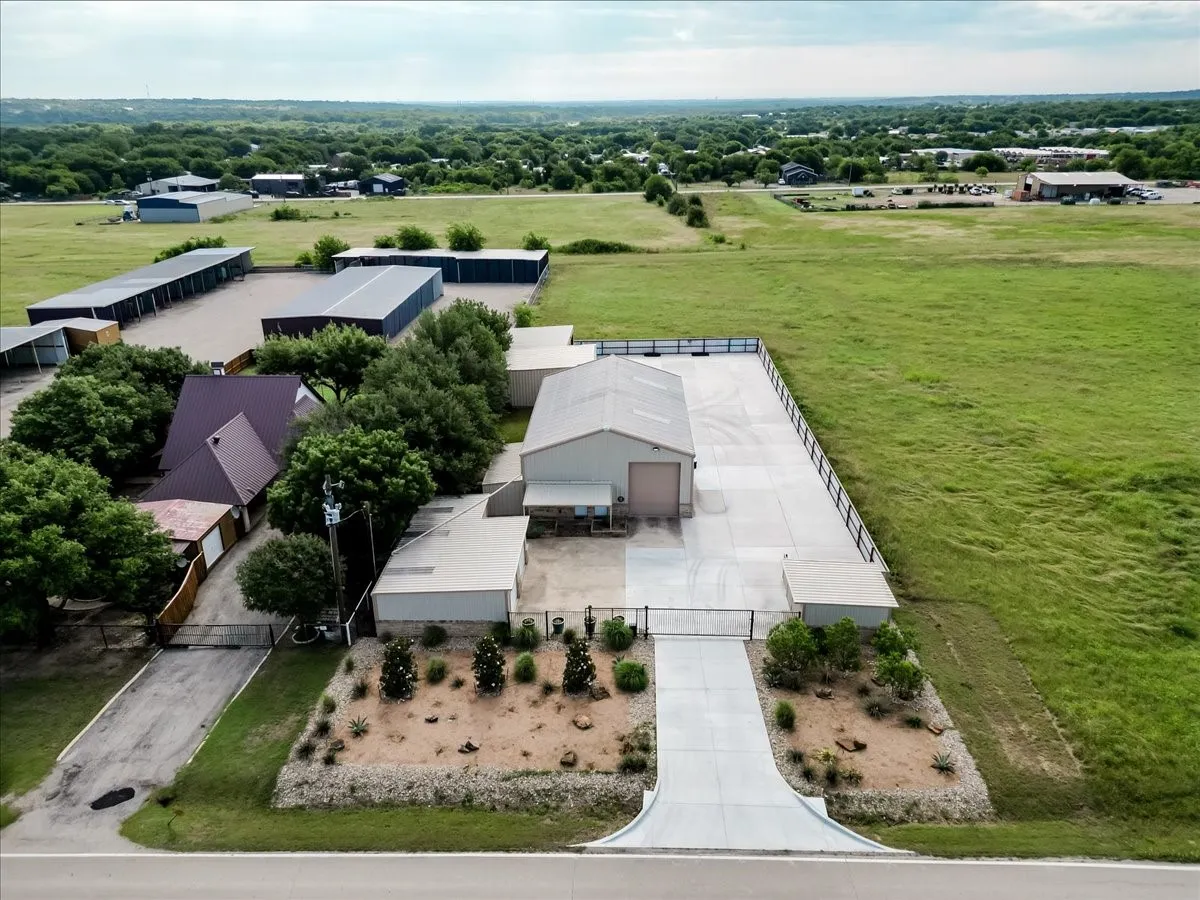 Entrance featuring multiple metal-sided structures, a concrete driveway, metal perimeter fencing, and professional xeriscaping