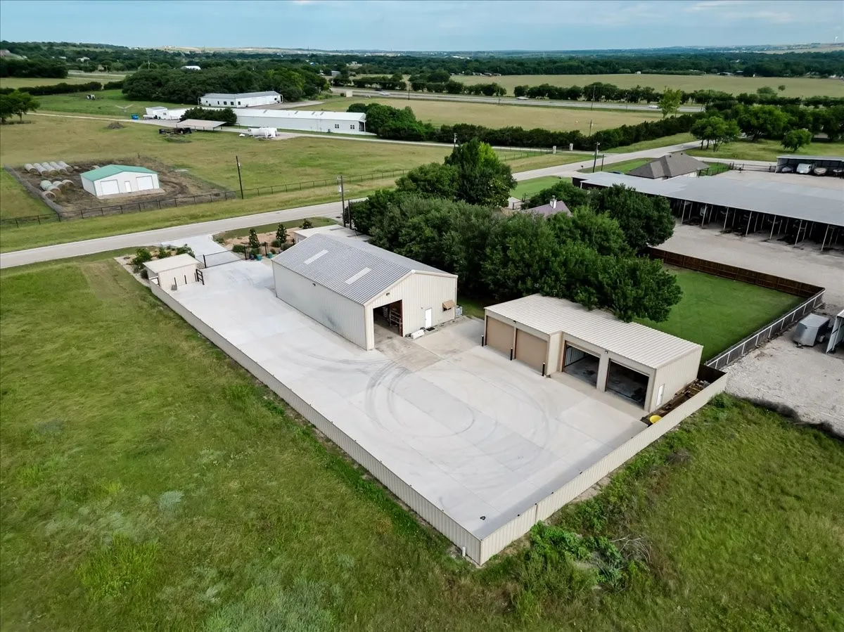 Expansive concrete apron, metal-sided workshop with a gabled roof, and a separate multi-bay garage structure situated on a fenced lot