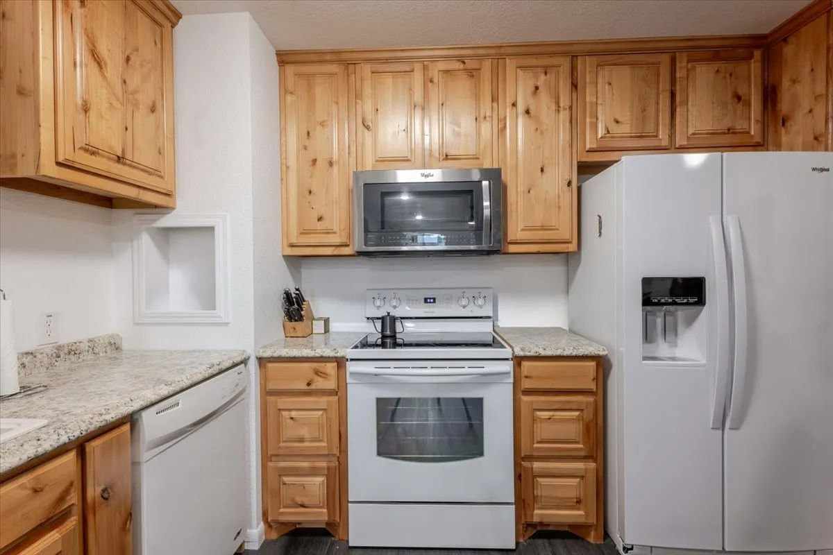 Breakroom featuring knotty wood cabinetry, light-toned stone-finish countertops, and a full suite of white appliances including a side-by-side refrigerator, smooth-top range, and built-in microwave